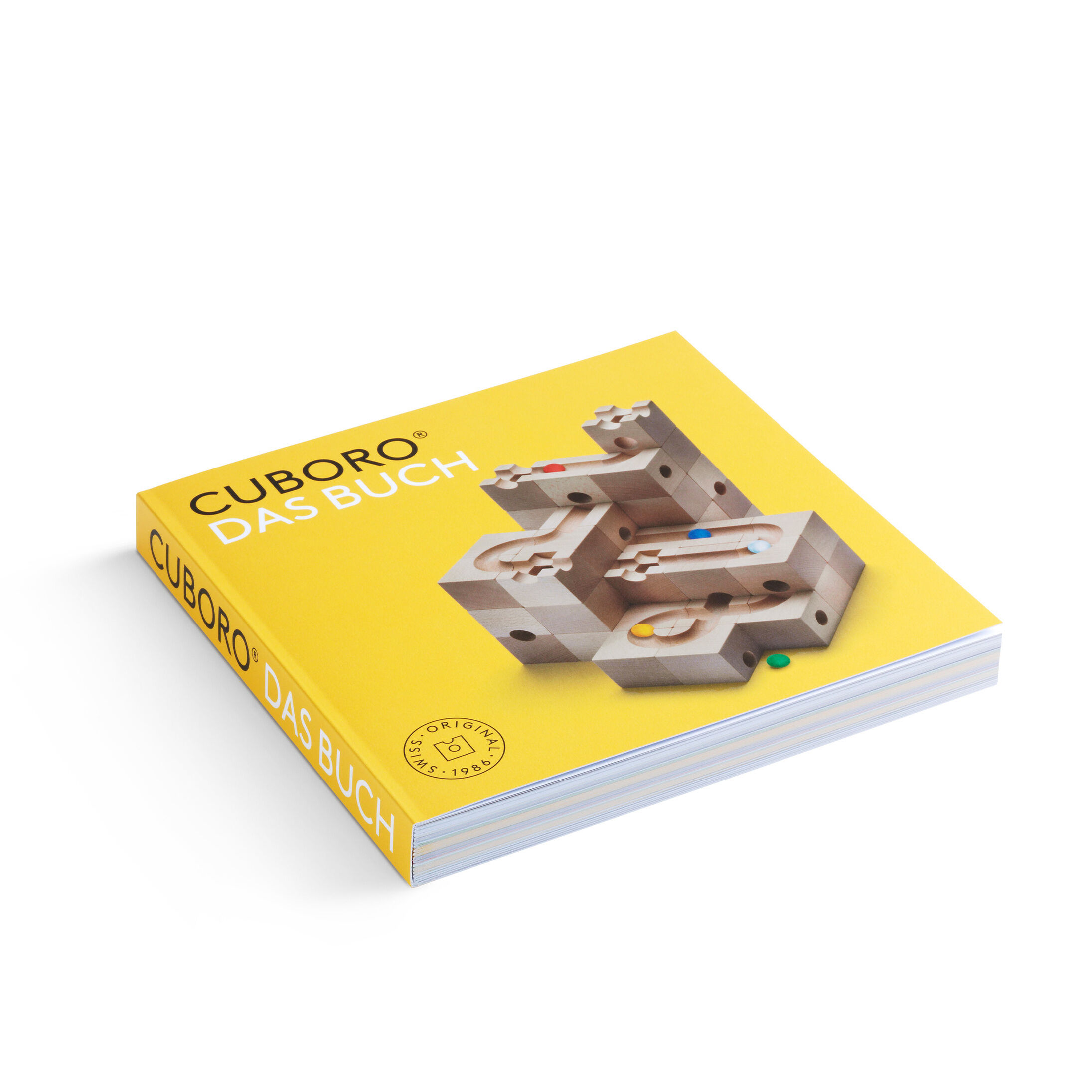 Quadratisches Buch mit gelbem Umschlag. Auf dem Cover steht der Titel „CUBORO - DAS BUCH“. Abgebildet ist eine Kugelbahn-Konstruktion aus Holz mit farbigen Kugeln. Das Buch wirkt hochwertig und ansprechend, ideal für kreative Bauideen und Herausforderungen rund um die Cuboro-Kugelbahn.