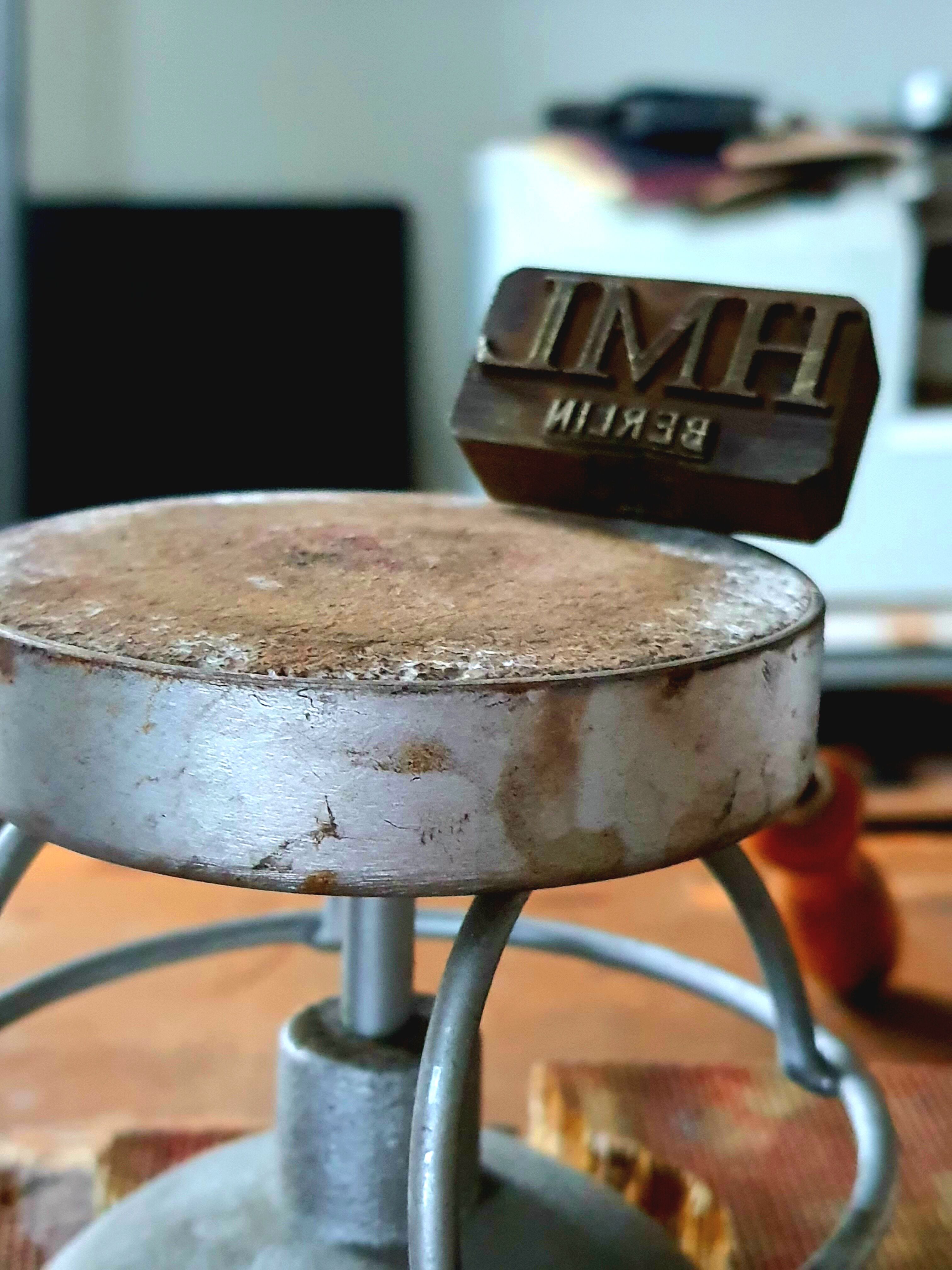 Abgenutzte runde Metallplatte auf einem Ständer, darüber ein Stempel mit der Aufschrift 'BERLIN'