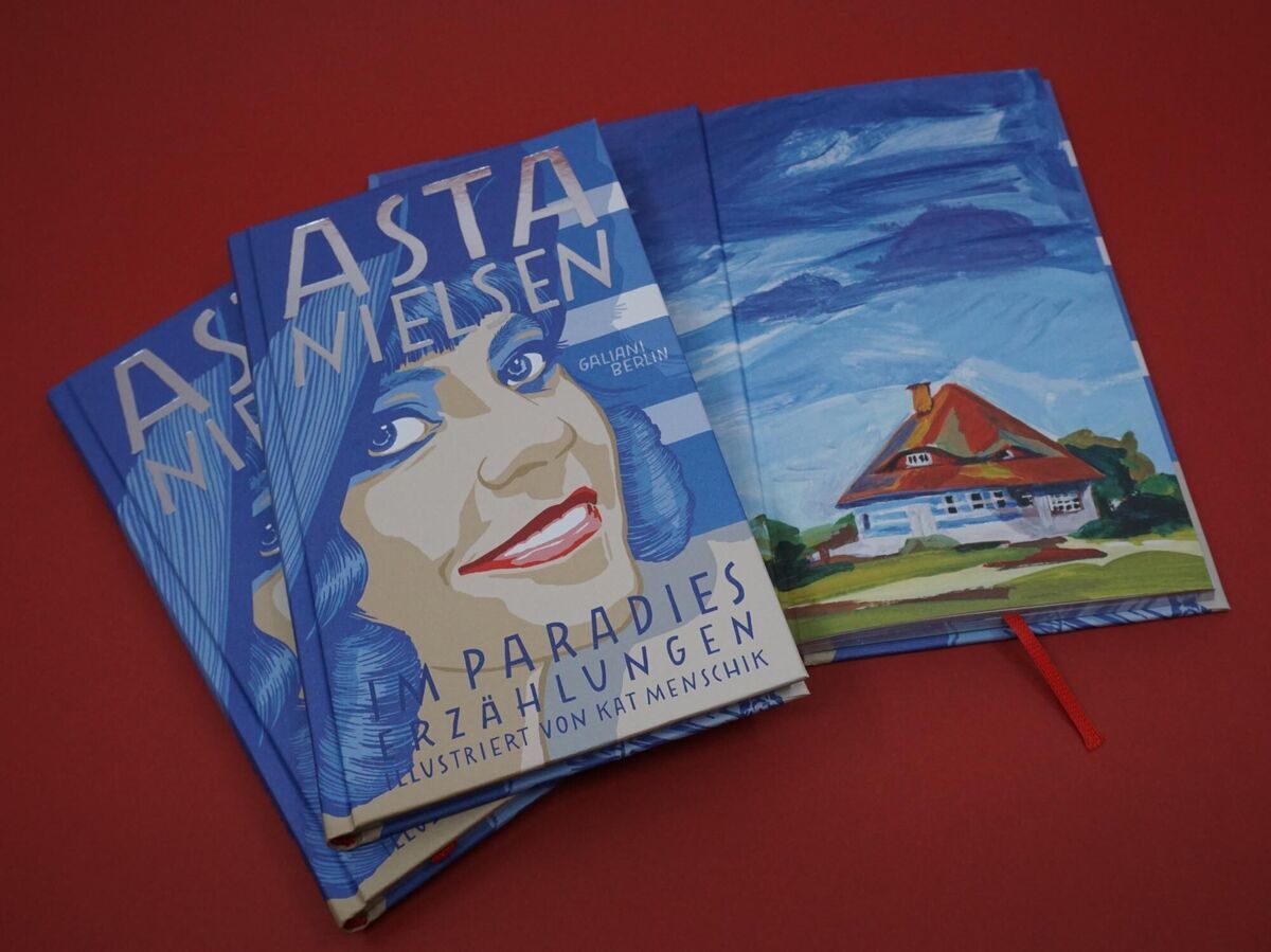 Mehrere Exemplare des Buches "Nielsen, Asta: Im Paradies" mit blauen Covern und Illustrationen, die eine Frau und ein Haus zeigen, auf einem roten Hintergrund liegend.