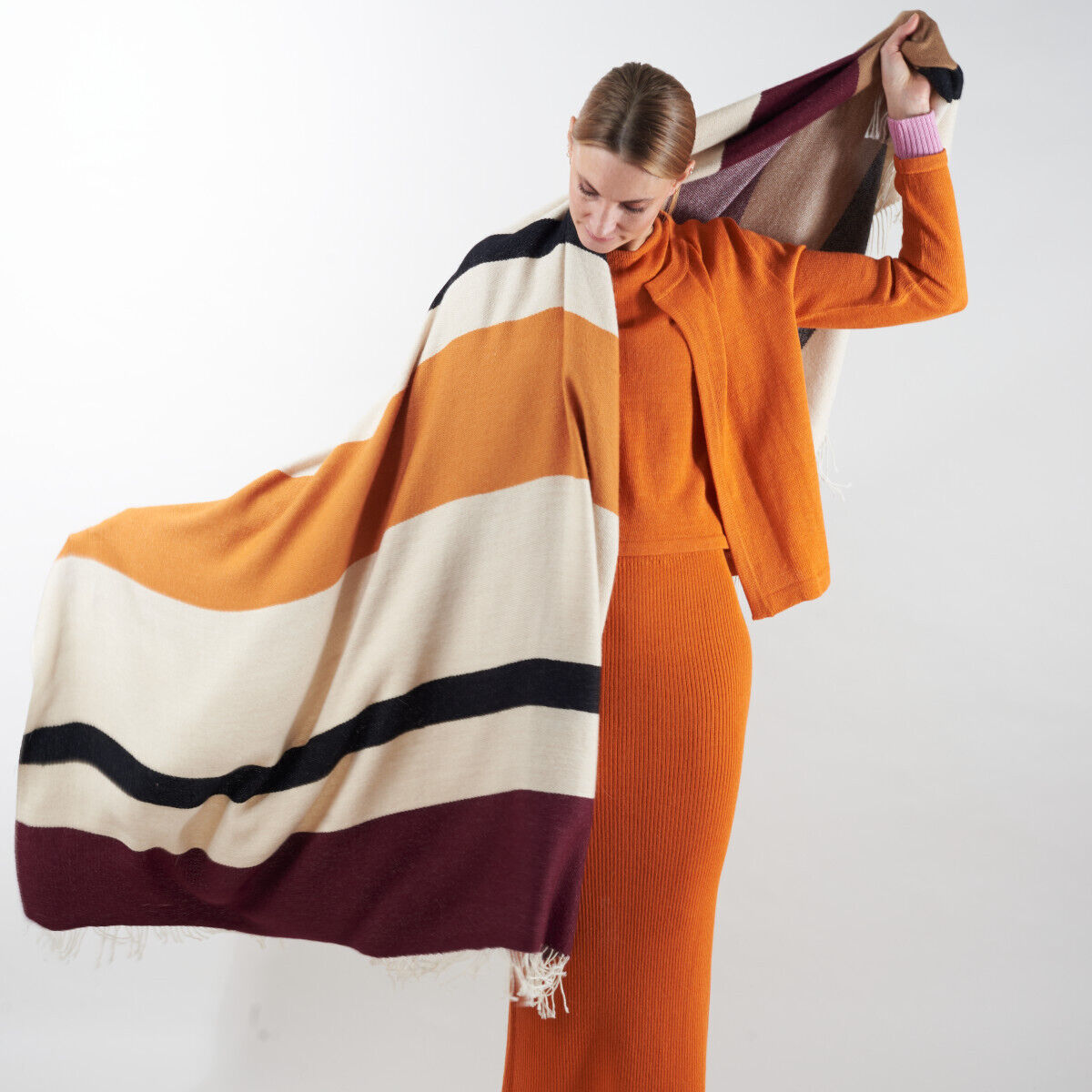 Frau trägt ein Cape aus Alpaka-Wolle in Orange, Weiß, Schwarz, Bordeaux und Beige.