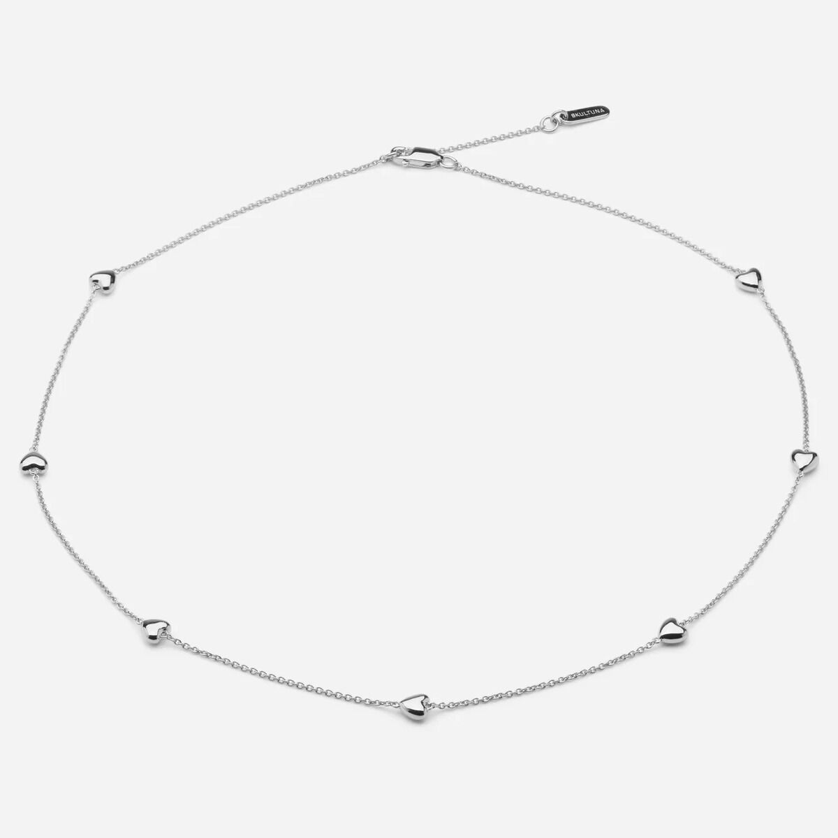 Das Bild zeigt eine zarte Collier-Halskette aus Sterling-Silber der Marke SKULTUNA MESSINGSBRUK. Die feine Kette ist gleichmäßig mit kleinen, herzförmigen Anhängern versehen und wirkt modern und elegant. Der Schmuck liegt auf hellem, neutralem Hintergrund.