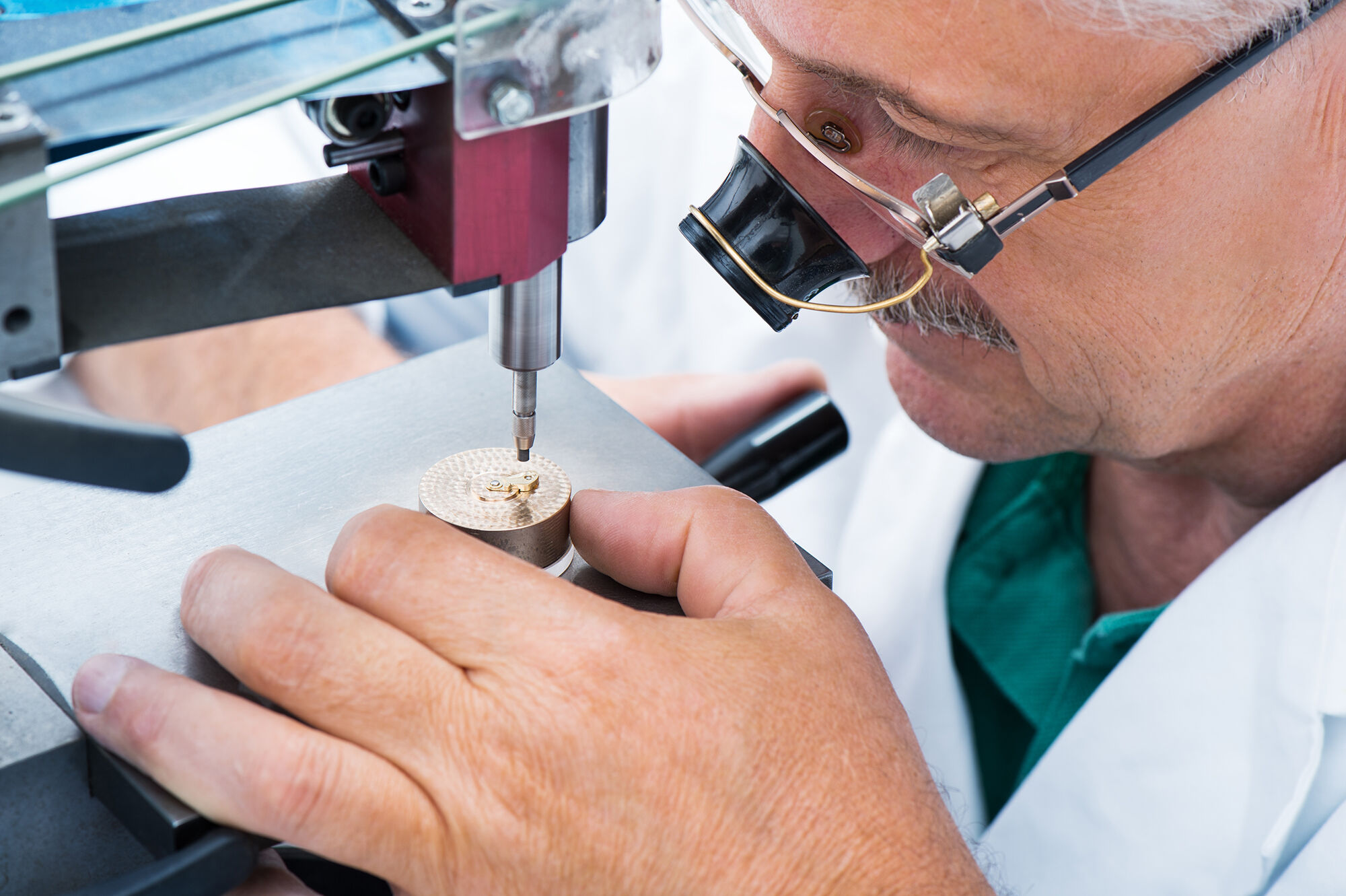 Ein Techniker arbeitet mit einem Präzisionsgravurwerkzeug an einem runden Goldstück, das er in einer Laborumgebung bis ins kleinste Detail prägt.