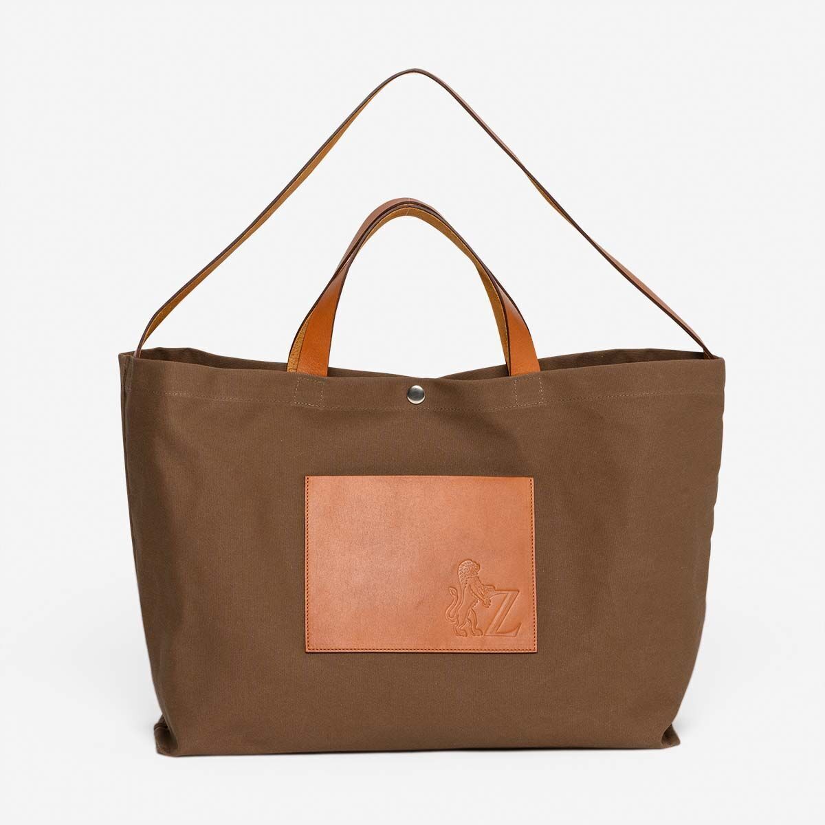 Eine Jubiläums-Markttasche aus braunem Stoff mit hellen Lederdetails und braunen Griffen im minimalistischen Design.