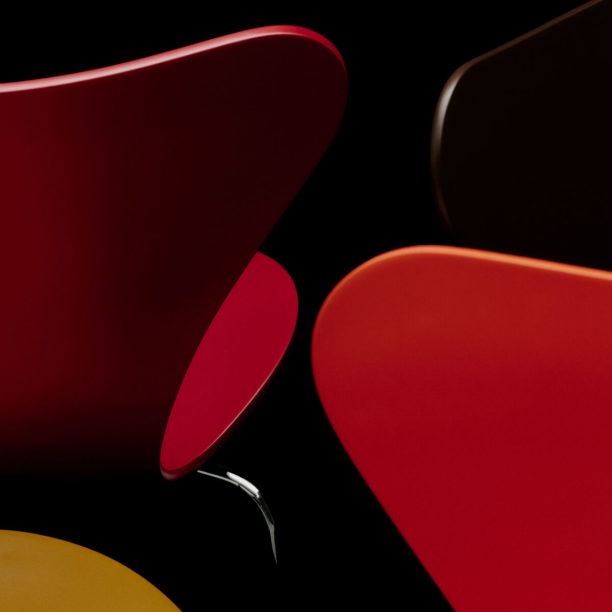 Detailansicht mehrerer Stühle der Serie 7, Edition Verner Panton von Fritz Hansen. Die Stuhlschalen in Orange, Gelb und Rot kontrastieren vor schwarzem Hintergrund, die modernen, geschwungenen Formen wirken hochwertig und ikonisch.