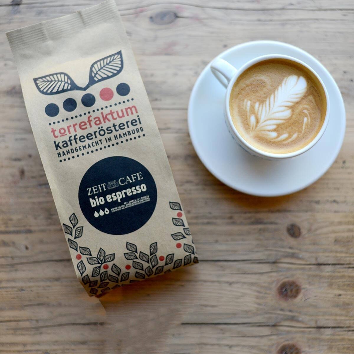 Verpackung der Bio-Espressobohnen »ZEITblend« von einer Kaffeerösterei in Hamburg und eine Tasse Latte Art auf Holztisch.