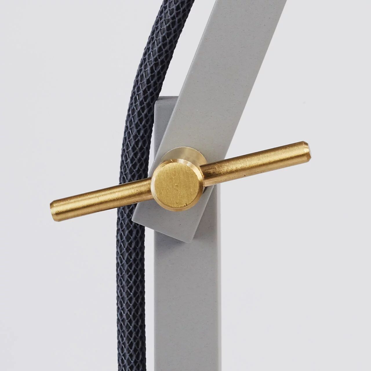 Detailaufnahme der Stehleuchte »schliephacke« von mawa design in Grau: Im Vordergrund ein mattgrauer Aluminiumarm, daran eine waagerechte Messingschraube mit Zylinderkopf befestigt. Dahinter verläuft ein schwarzes, textilummanteltes Stromkabel. Der Hintergrund ist neutral hellgrau.