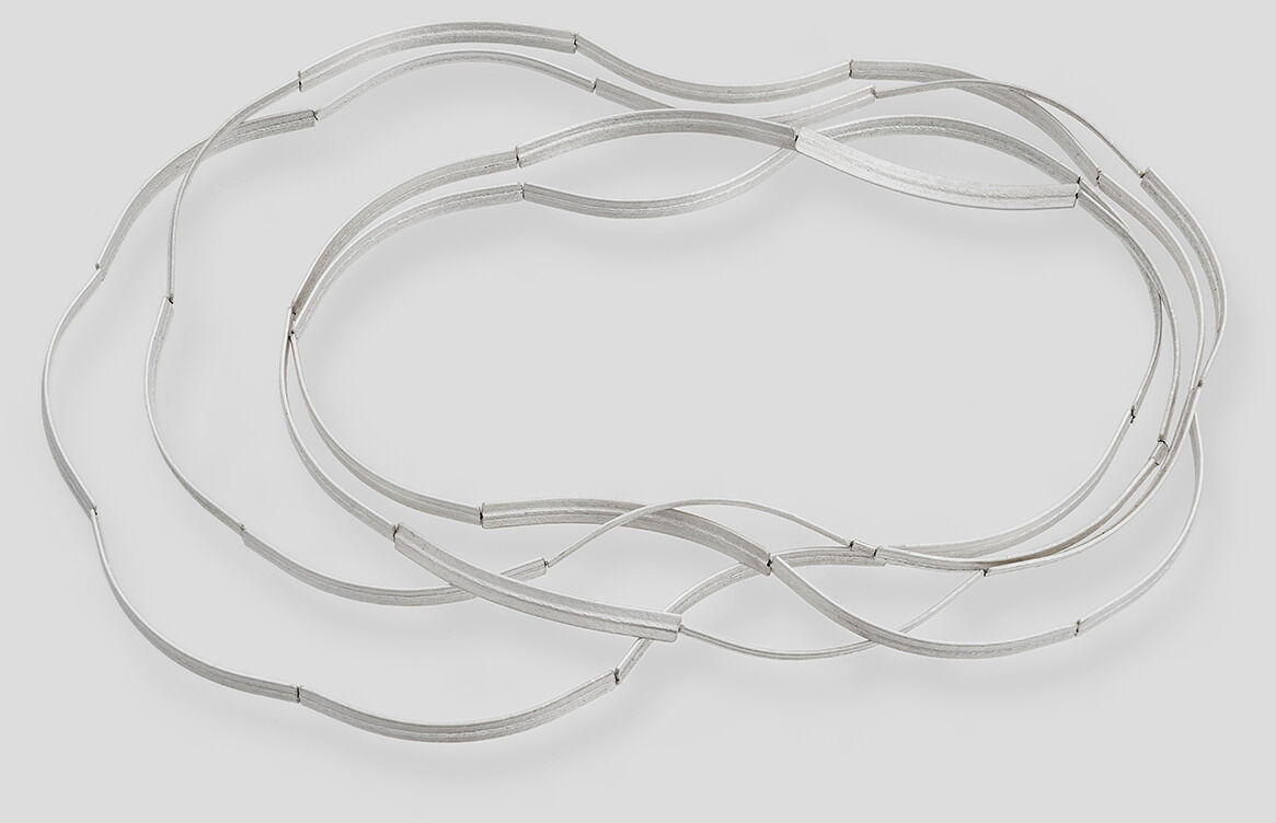 Eine zarte Kette aus Silber mit einem eleganten, geschwungenen Design, die auf einem hellen Hintergrund liegt.