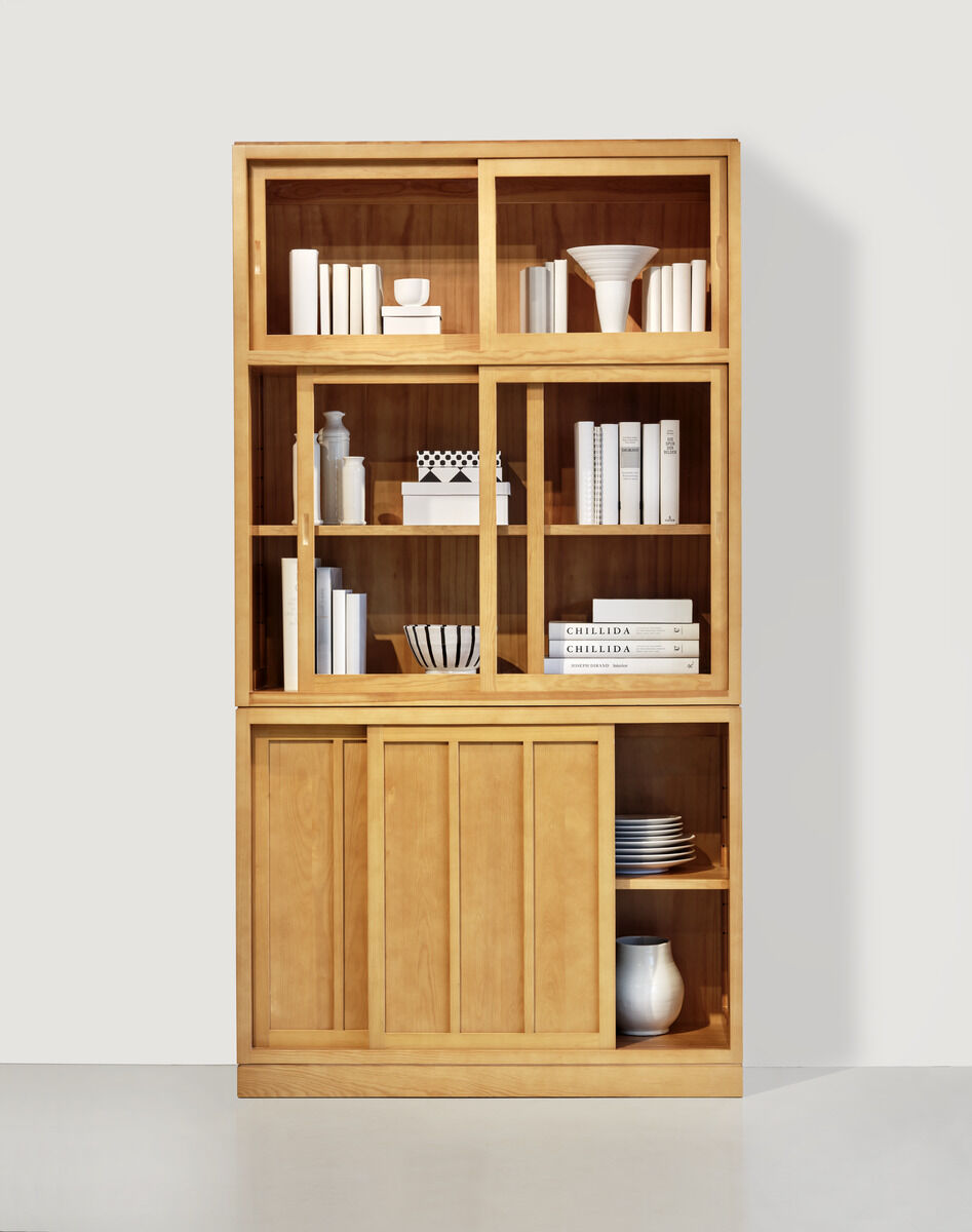 ZEIT-Sonderedition Vitrine »Multimodus« in hellem Holz. Sie hat offene und geschlossene Regale, dekoriert mit verschiedenen Büchern, Vasen und anderen Einrichtungsgegenständen. Das Design ist modern und minimalistisch.