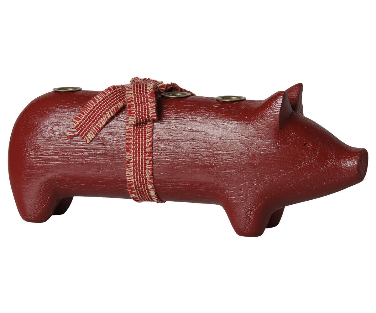 Mittlerer, roter Kerzenhalter in der Form eines Schweins aus Holz der Marke Maileg. Auf dem Rücken befinden sich drei Kerzentüllen aus Metall. Das Schwein ist mit einem roten Stoffband und Schleife dekoriert. Glatte, matte Oberfläche, rustikaler Stil.