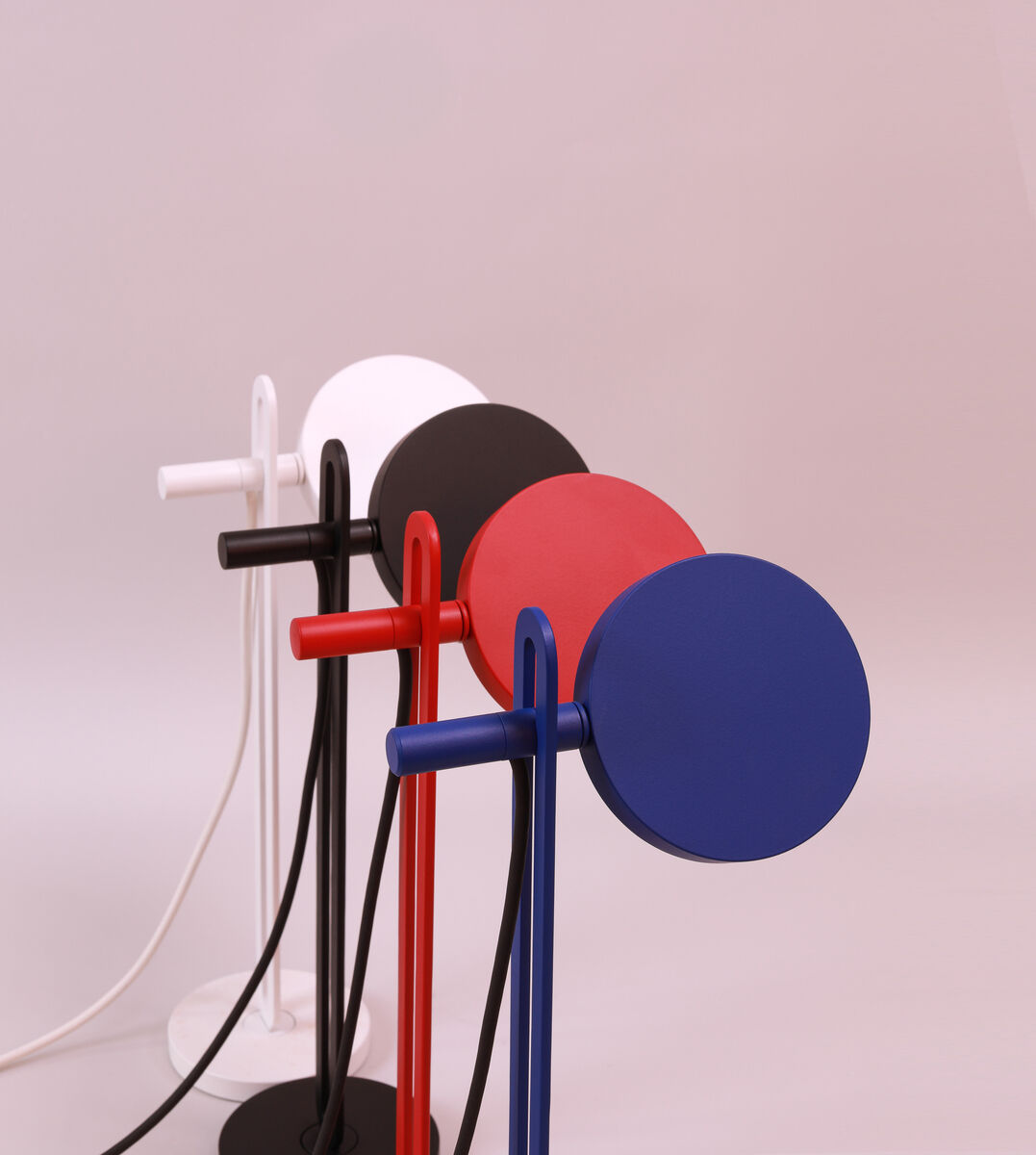 Eine Tischlampe namens 'Echo' in verschiedenen Farben: Blau, Rot, Schwarz und Weiß. Die Lampen haben ein modernes, minimalistisches Design und sind in einer Reihe aufgestellt.