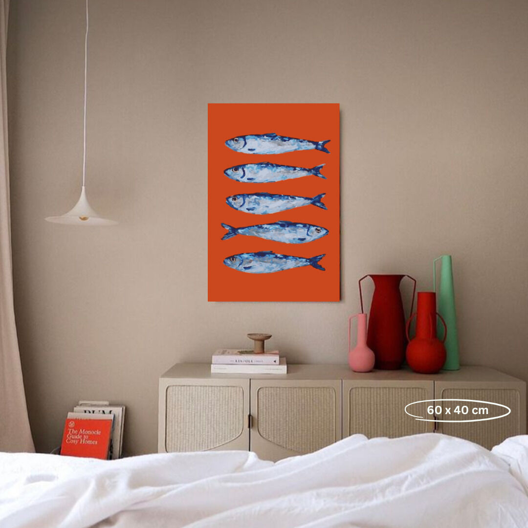 Malen nach Zahlen Bild mit dem Titel 'Perspektivwechsel', zeigt fünf blaue Fische auf rotem Hintergrund. Das Bild hängt an einer beigen Wand über einem Schrank, auf dem Bücher und dekorative Vasen stehen. Ein minimalistisches, modernes Wohnambiente.