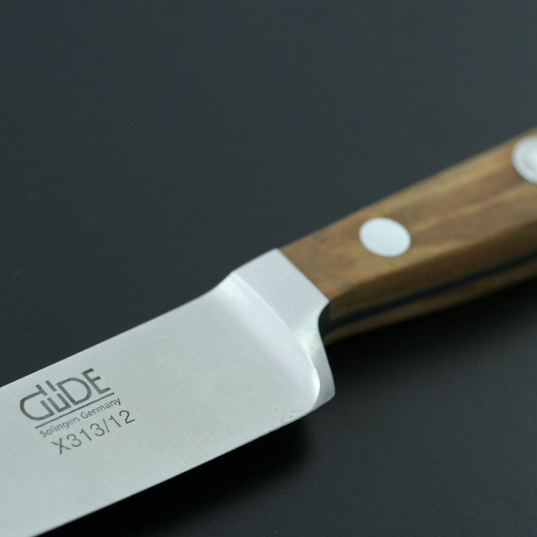 Nahaufnahme eines Spickmessers mit einer Klinge aus Edelstahl und einem Griff aus Olivenholz auf einem dunklen Untergrund.