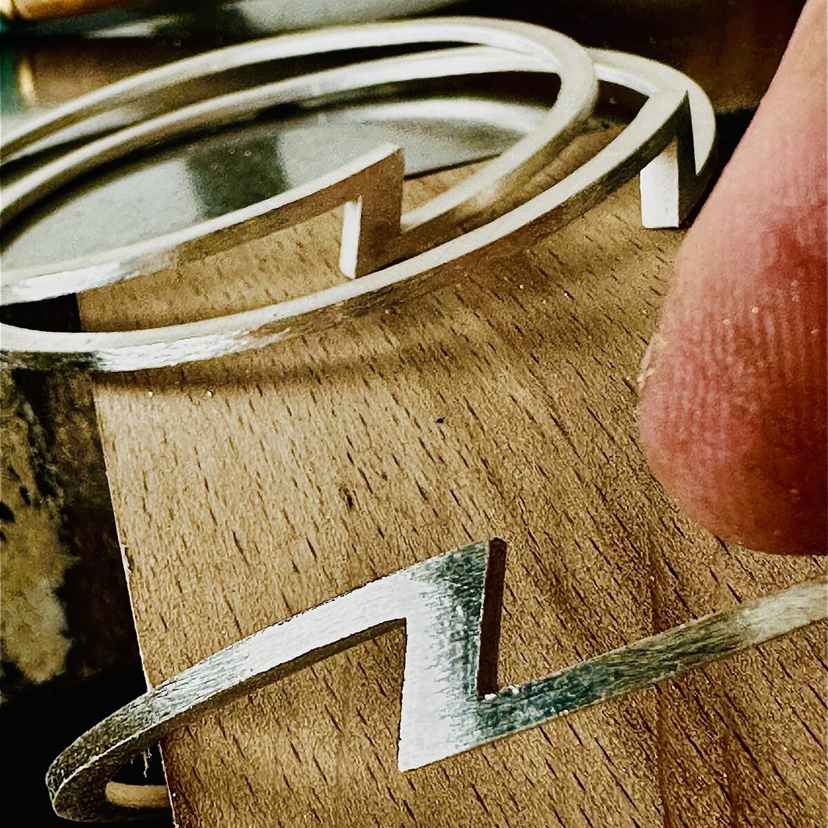 Nahaufnahme von zwei silbernen Armreifen der ZEIT Sonderedition von HML Berlin auf einer Holzoberfläche. Im Hintergrund liegt ein Holz-Werkzeug. Ein charakteristisches Zickzack-Design ist auf den Armreifen zu sehen, das Material wirkt matt und hochwertig verarbeitet.