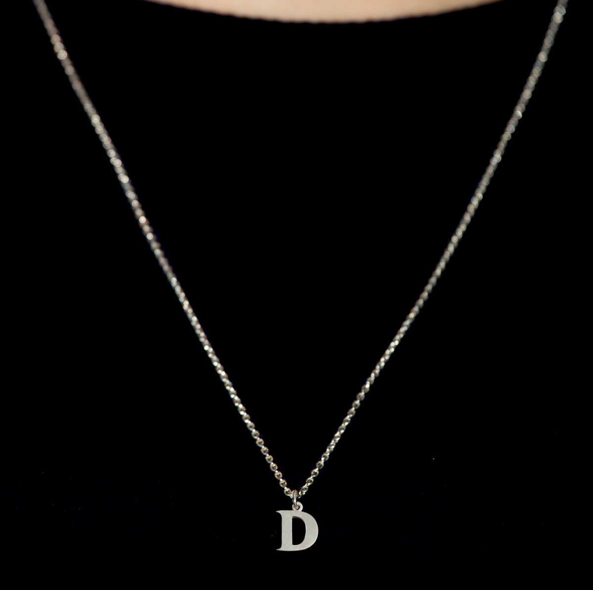 Nahaufnahme einer feinen Silberkette mit einem Buchstabenanhänger "D" gegen einen schwarzen Hintergrund.
