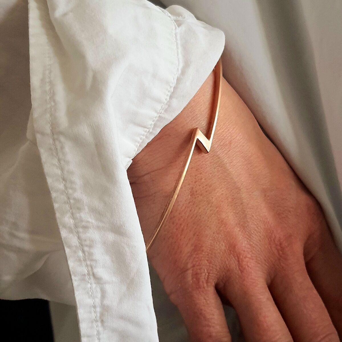 Goldfarbener Armreif mit modernem, minimalistischem Design am Handgelenk einer Person in einem weißen Hemd.