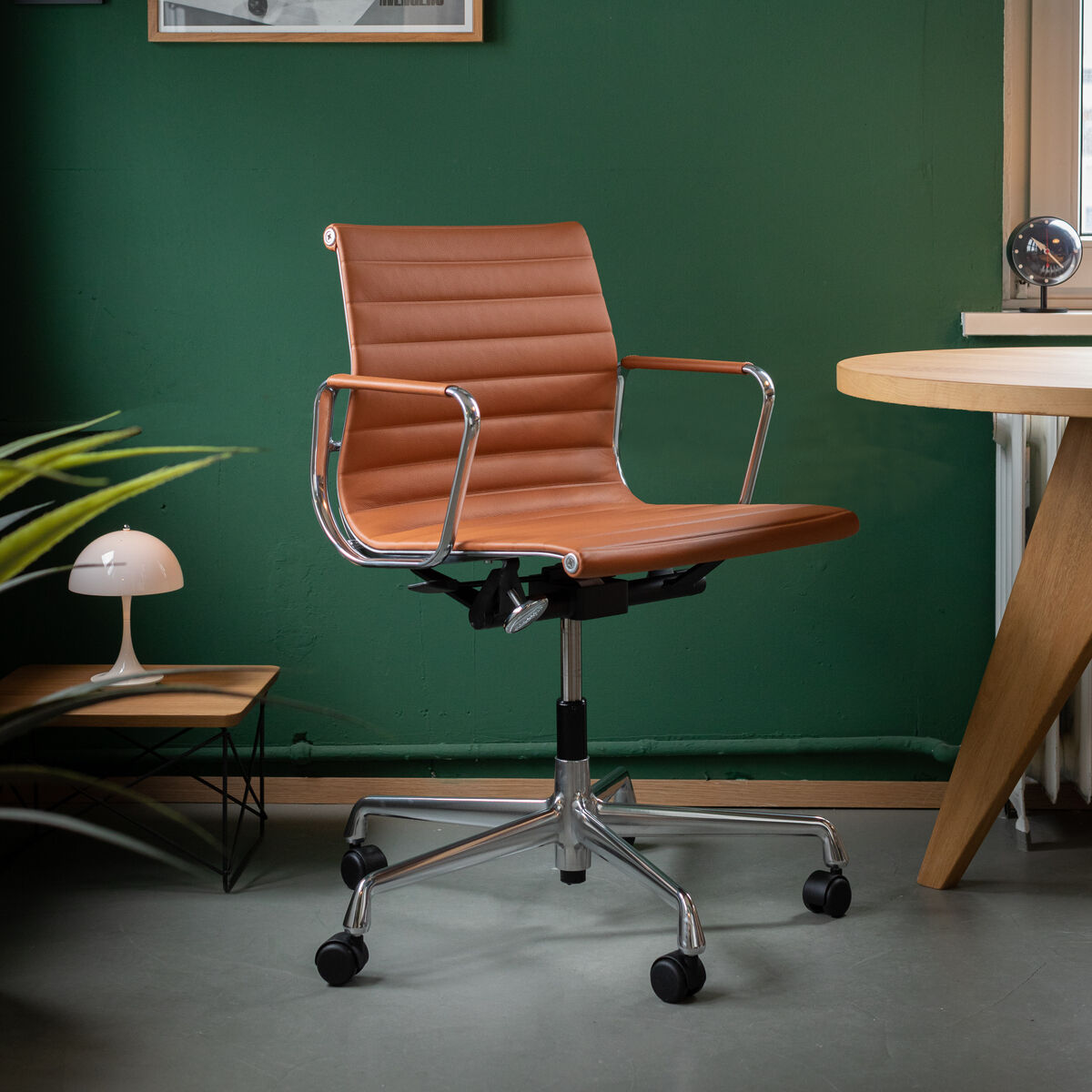 Brauner Vitra Alu Chair EA 118 Drehstuhl vor einer grün gestrichenen Wand, dekoriert mit Bildern und einem weißen Schreibtisch in einem modernen Büro.