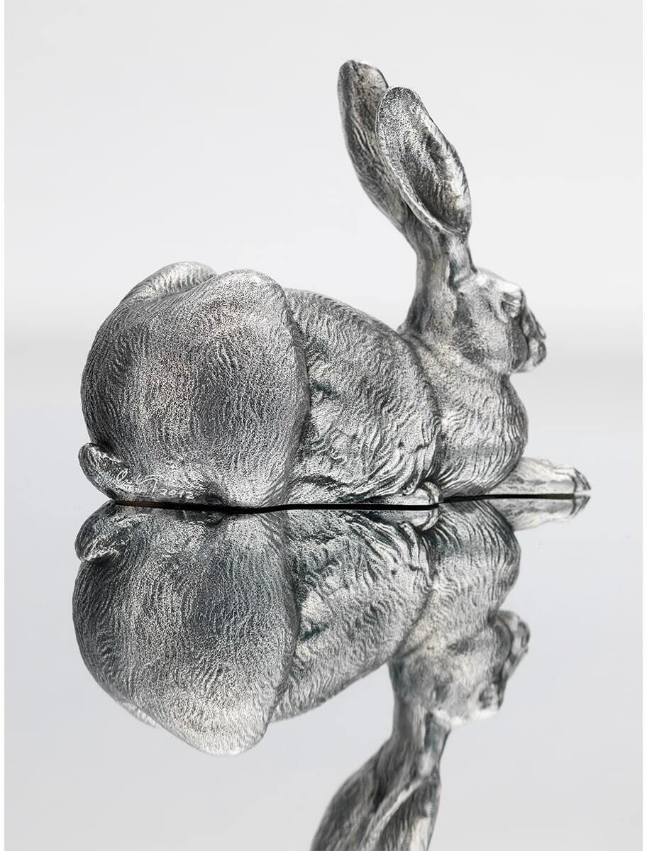 Hörl, Ottmar: Skulptur »Dürer-Hase«, 2012. Eine detailreiche silberne Hasenfigur, die auf einer glänzenden Oberfläche ruht, wobei sich die Figur im Untergrund spiegelt. Die Skulptur zeigt den Hasen in liegender Position, inspiriert von Albrecht Dürers berühmtem Hasen.