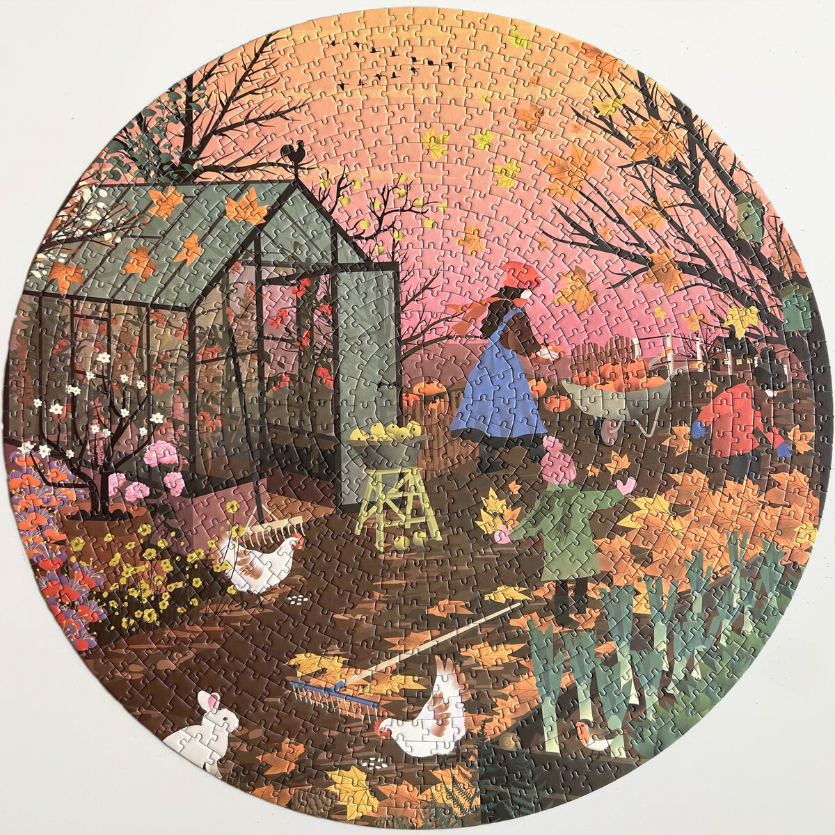 Ein rundes Puzzle mit herbstlicher Gartenszene. Im Vordergrund sind Hühner, ein Hund, Pflanzen und herabgefallenes Laub zu sehen. Eine Person arbeitet im Garten nahe eines Glashauses. Die dominante Farbpalette besteht aus warmen Herbstfarben wie Orange, Braun und Rot sowie grünen und rosa Akzenten.