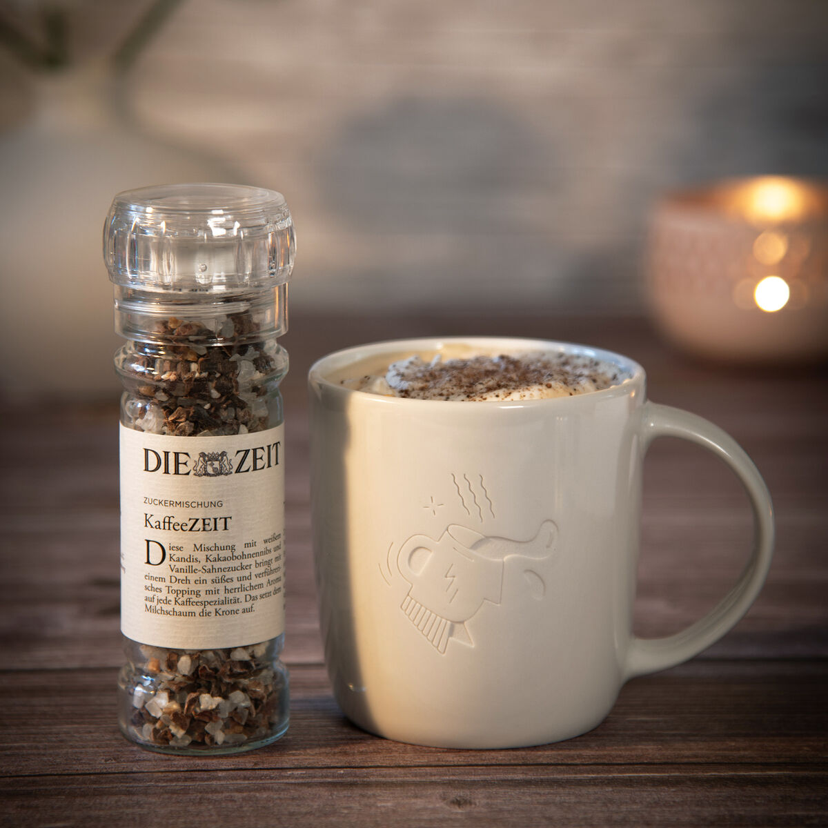 Ein Geschenkset bestehend aus einer Tasse mit der Aufschrift 'Alles Gesagt' und einem Glas Kaffeezeit-Gewürzmischung. Die Produkte sind auf einem Holztisch mit unscharfem Hintergrund und warmen Licht abgebildet.