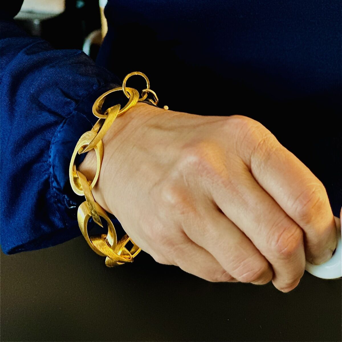 Nahaufnahme eines feingoldplattierten silbernen Armbands am Handgelenk einer Person in einem blauen Oberteil.