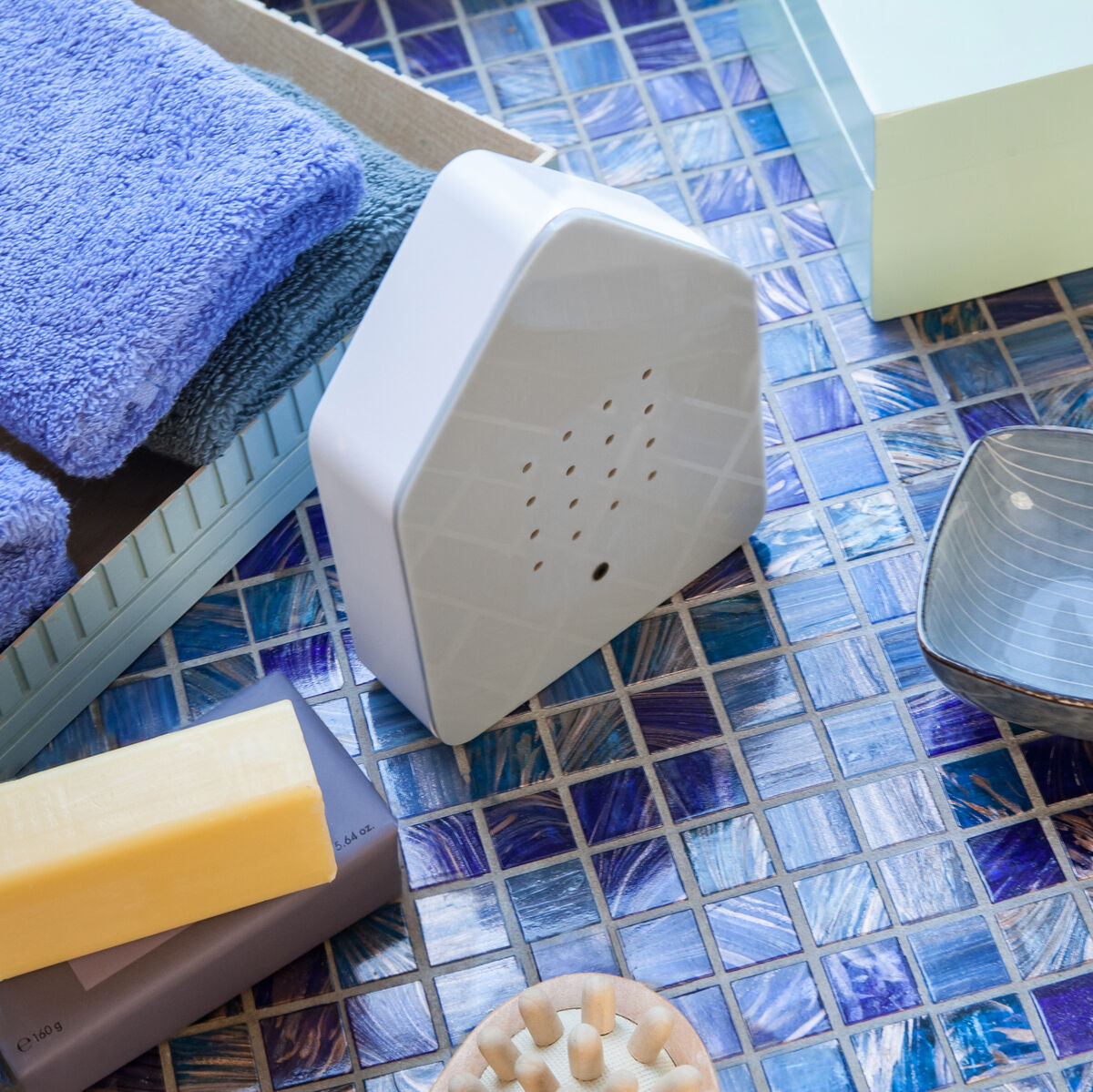 Eine Zwitscherbox auf einem blau-türkisen Fliesenhintergrund mit Handtüchern, einer Seife und Dekorationsartikeln.