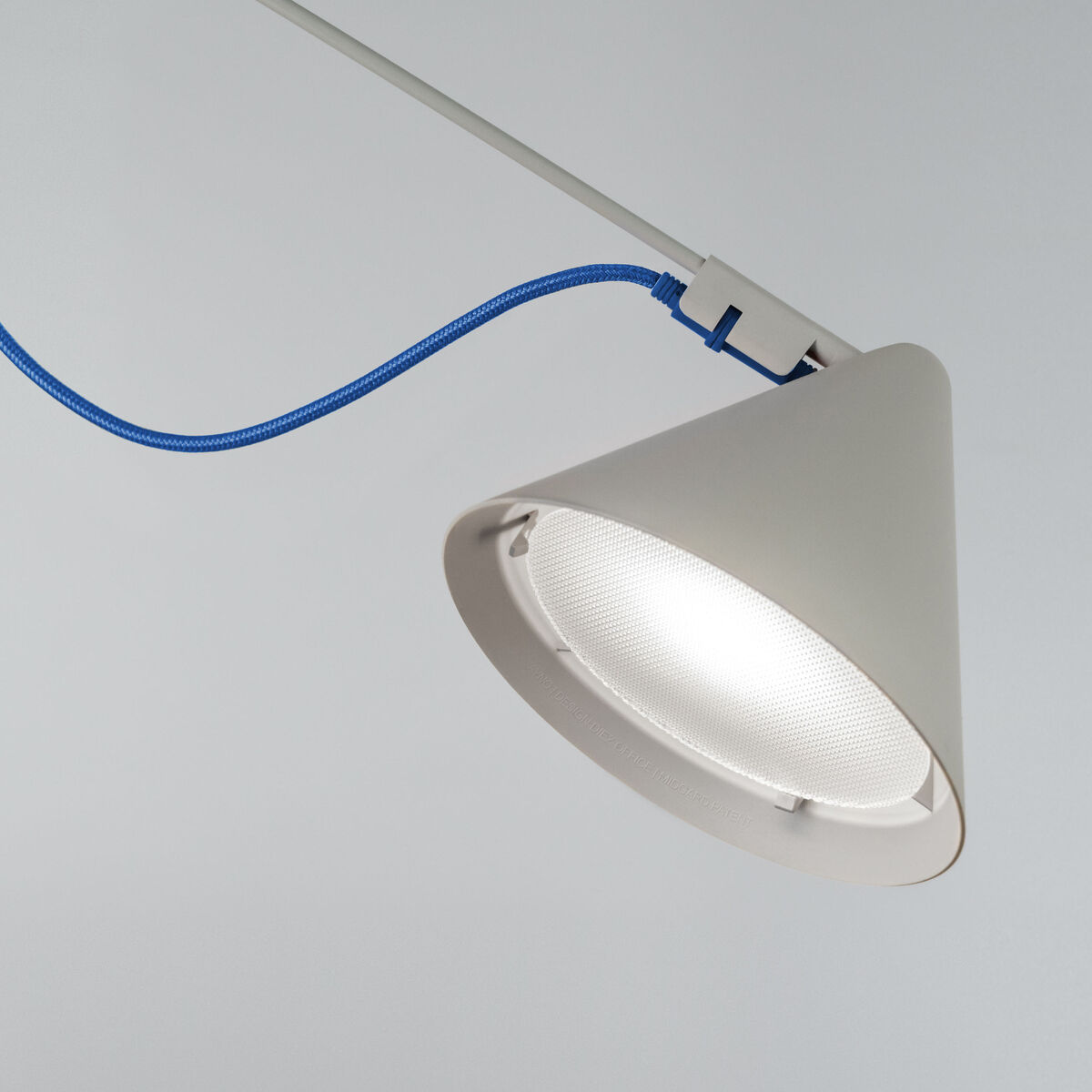 Nahaufnahme einer modernen Stehlampe der ZEIT-Sonderedition AYNO, mit konisch geformtem weißen Lampenschirm und markantem ultramarinblauen Stromkabel vor neutral grauem Hintergrund.