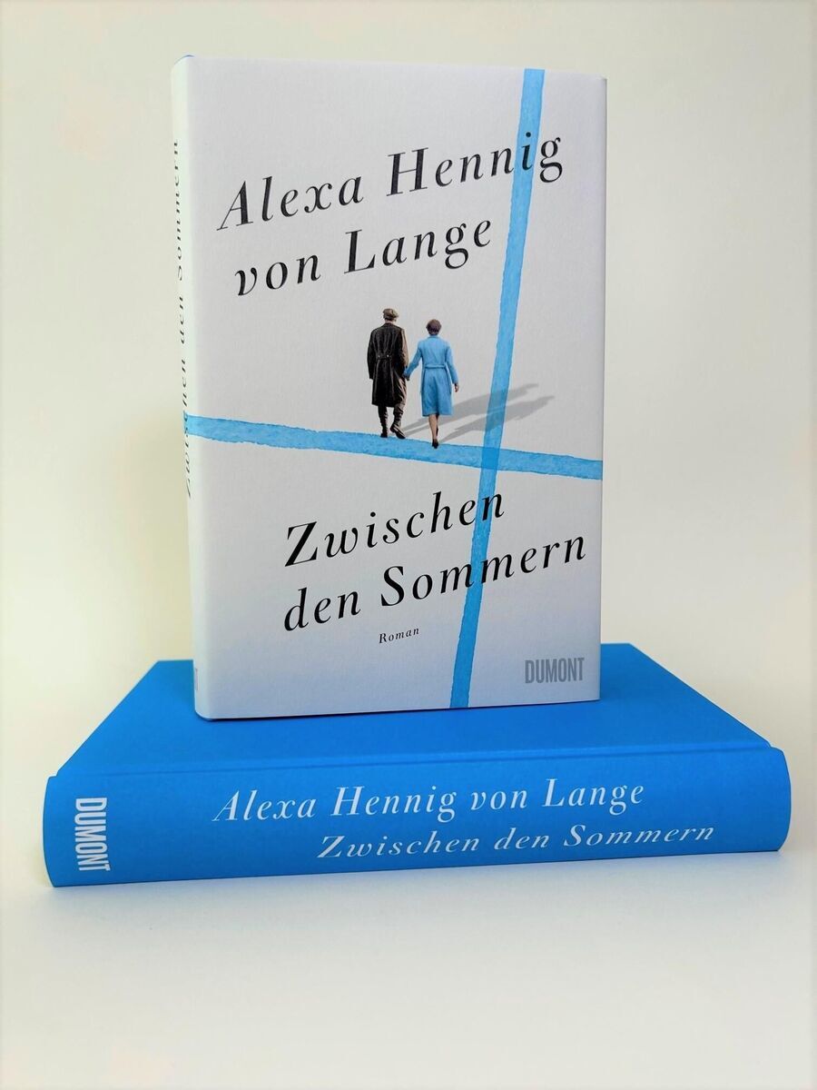 Das Bild zeigt das Buch 'Zwischen den Sommern' von Alexa Hennig von Lange, veröffentlicht vom Dumont Verlag. Das Buchcover zeigt zwei Personen, die auf einer hellen Oberfläche spazieren gehen, wovon einer in einem schwarzen und der andere in einem blauen Mantel gekleidet ist. Das Buch liegt auf einem blauen Buchrücken, auf dem der Titel und der Name der Autorin ebenfalls zu lesen sind.