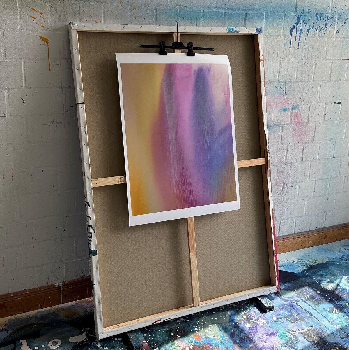 Ein Kunstdruck von Paul Schrader mit dem Titel „Miami No. 3“, Teil der ZEIT Sonderedition. Das Bild zeigt eine abstrakte Komposition in lila, gelben, blauen und rosa Farbtönen. Es ist auf einer Holzstaffelei vor einer weißen Backsteinwand ausgestellt, mit einem farbenreichen Boden darunter.