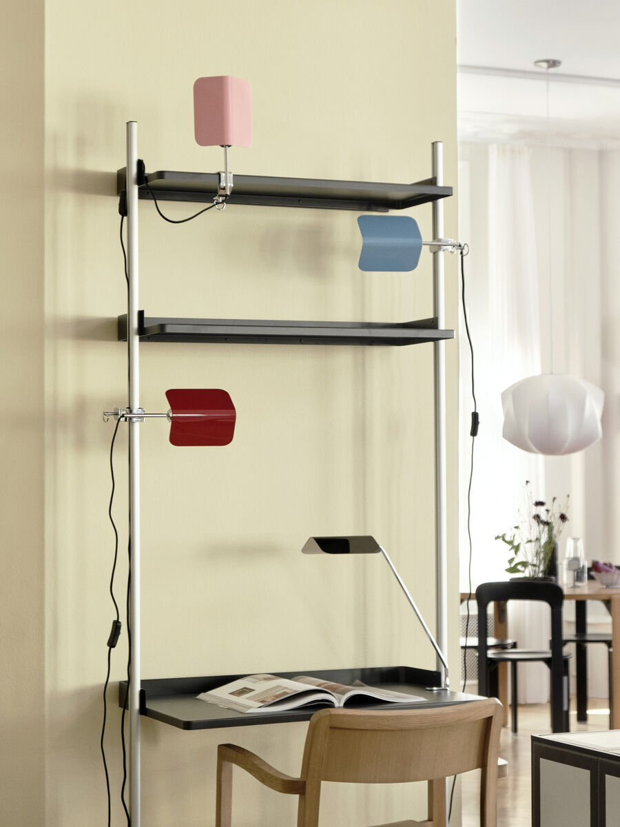 Ein Bild zeigt drei Apex Lampen »Clip« auf einem schwarzen Regal und einem Schreibtisch in einem modernen Wohnumfeld. Die Lampen sind in den Farben rot, blau und rosa dargestellt.