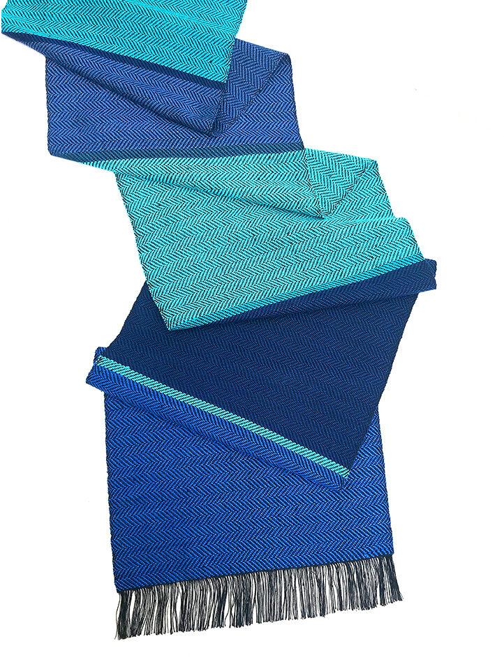 Eleganter Seidenschal in den Farben Blau und Türkis mit dezentem Herringbone-Muster und schwarzen Fransen an den Enden.