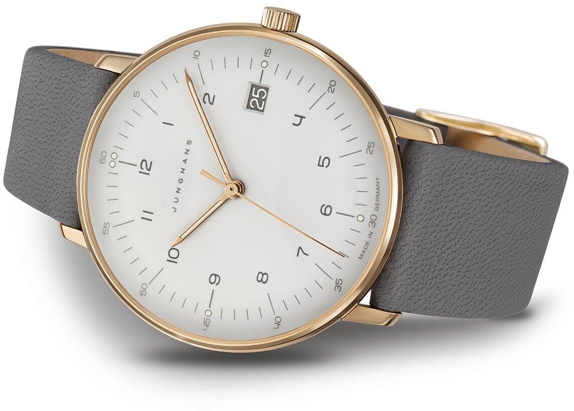 Zeigt eine ZEIT-Sonderedition 'max bill Damen' Armbanduhr von Junghans mit einem goldenen Gehäuse, einem grauen Lederarmband und einem weißen Zifferblatt mit minimalistischen Design.