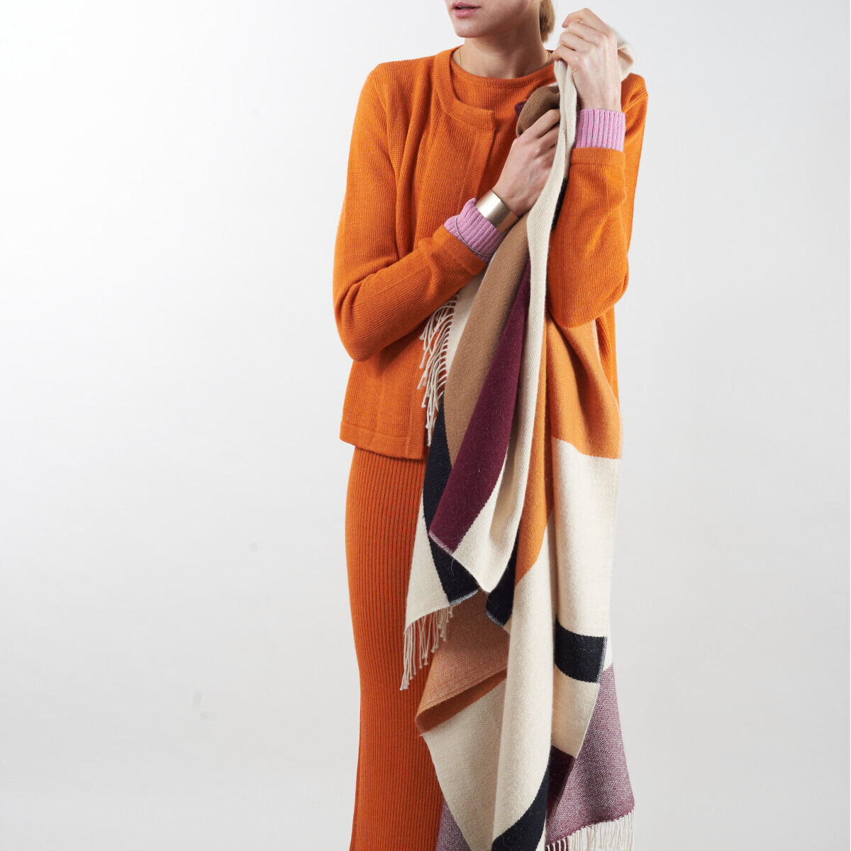 Person trägt ein Cape aus Alpaka-Wolle in Orange mit einem farbigen Jacquardmuster in Beige, Schwarz und Rot. Ideal für kalte Tage und verschiedene festliche Anlässe.
