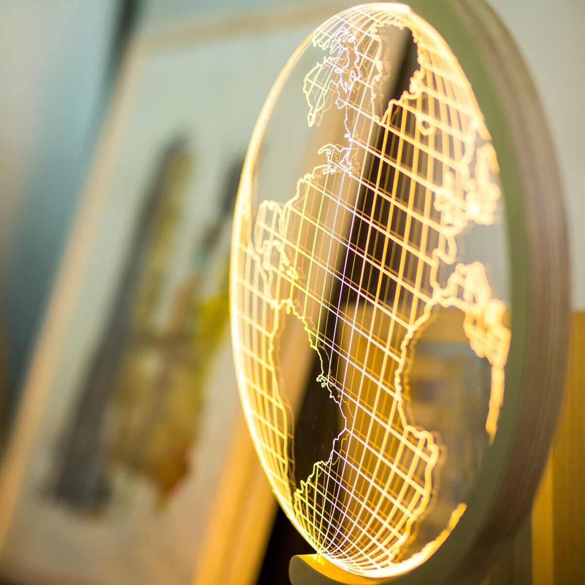 Eine LED-Leuchte in Form eines Globus, die auf einem Schreibtisch steht. Die Weltkarte ist in gelb-goldenen Leuchtlinien dargestellt. Der Hintergrund ist leicht unscharf und zeigt weitere Dekorationsgegenstände.