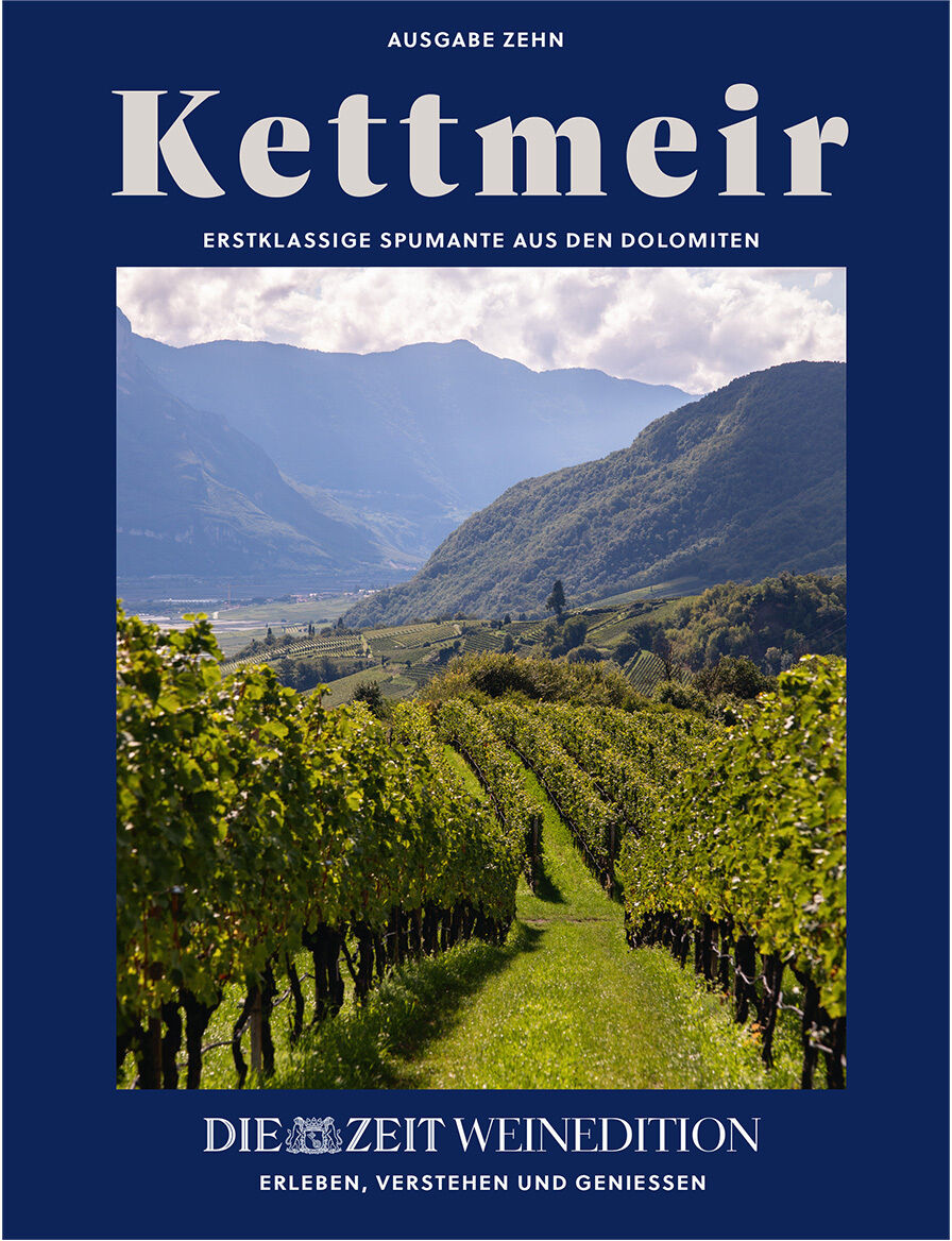Das Cover zeigt einen Weinberg in Südtirol mit Reihen von Reben vor einer Gebirgskette der Dolomiten. Oben prangt groß der Titel „Kettmeir“, darunter „Erstklassige Spumante aus den Dolomiten“. Unten steht „DIE ZEIT WEINEDITION“. Elegantes blaues Rahmen-Design.