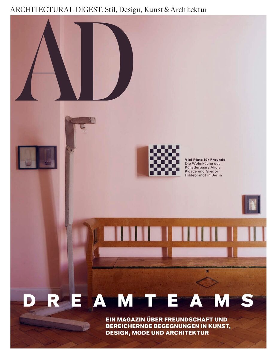 Cover der AD Architectural Digest mit dem Titel 'DREAMTEAMS'. Zu sehen sind eine vintage Holzbank, eine altmodische Waage und minimalistische Wandkunst mit Schachbrettmuster vor rosafarbener Wand. Thema: Freundschaft in Kunst, Design und Architektur.