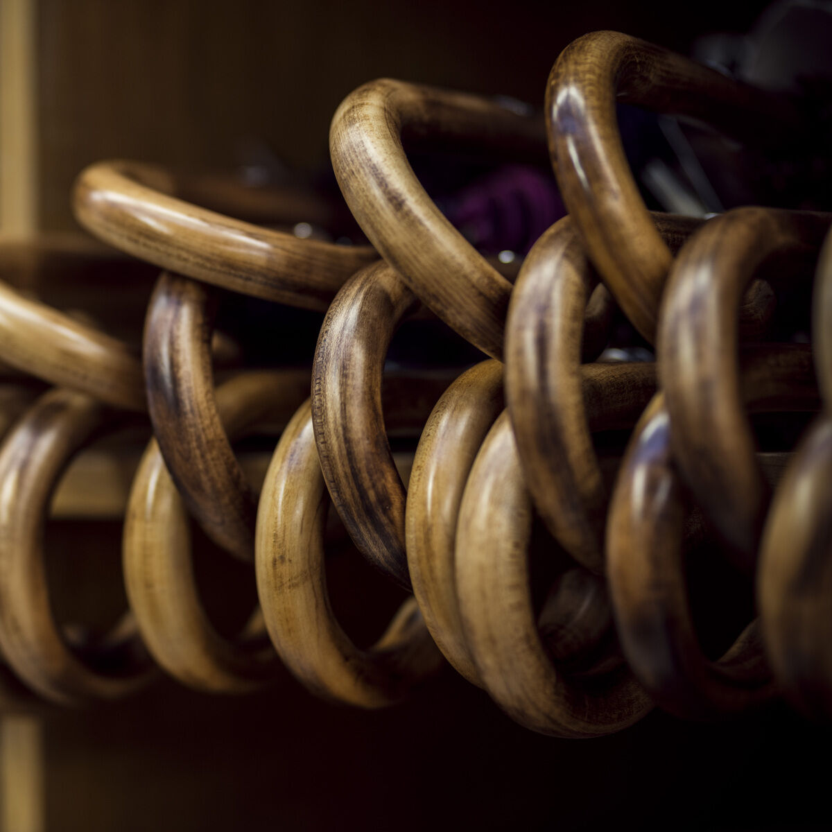 Nahaufnahme von mehreren ineinander verschlungenen Holzringen, vermutlich dekorative Gardinenringe, auf einem Regal liegend. Die Oberfläche der Ringe ist glatt und glänzend, verschiedene Brauntöne sind zu erkennen.