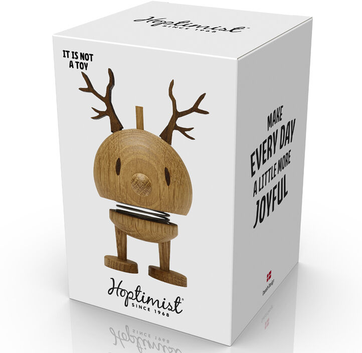 Abgebildet ist eine Hoptimist Rentier Bumble Figur aus Eiche. Die dekorative Holzfigur zeigt ein stilisiertes Rentier mit abgerundetem Körper, kleinen Beinen, auffälligen Geweihdetails sowie einem freundlichen Ausdruck. Die Verpackung ist weiß mit Produktfoto, typografischen Elementen und Motivationsbotschaften bedruckt. Das Design wirkt modern und minimalistisch, passend für winterliche oder festliche Dekorationen zu Weihnachten.