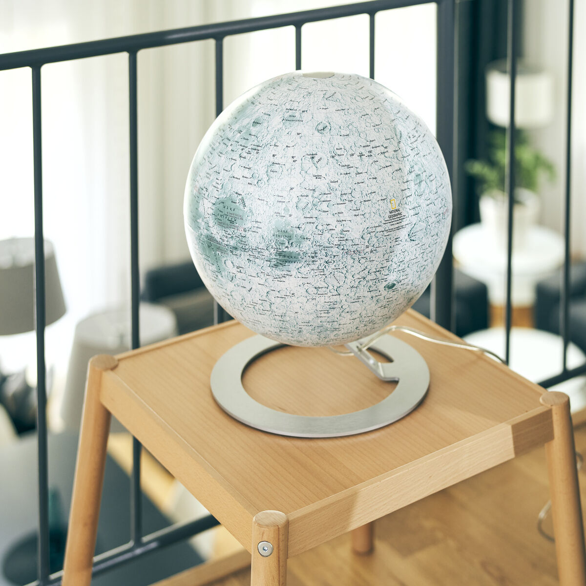 Ein Leuchtglobus von National Geographic „The Moon“ auf einem Holztisch im Wohnzimmer, der die Oberfläche des Mondes zeigt. Im Hintergrund sind ein Sofa und andere Einrichtungsgegenstände zu sehen.