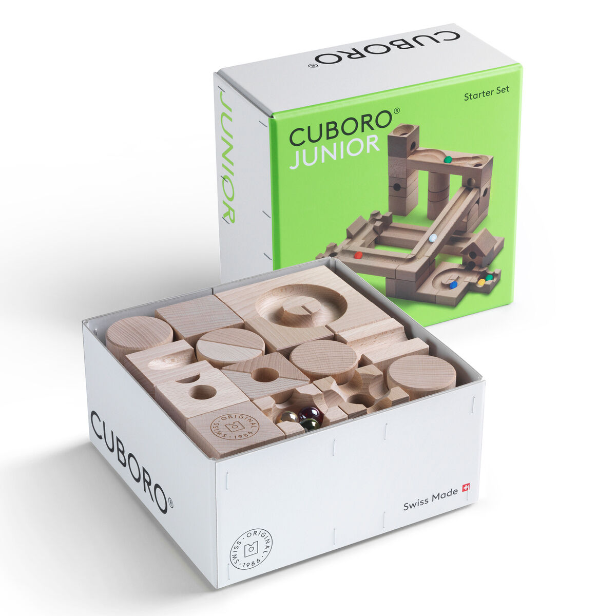 Das Bild zeigt das Kugelbahn Starter-Set »JUNIOR« von Cuboro. Im Vordergrund ist ein geöffneter, weißer Karton zu sehen, der 40 helle Holzelemente und 6 silberne Kugeln enthält. Dahinter steht die grüne Produktverpackung mit einer Abbildung einer aufgebauten Kugelbahn.