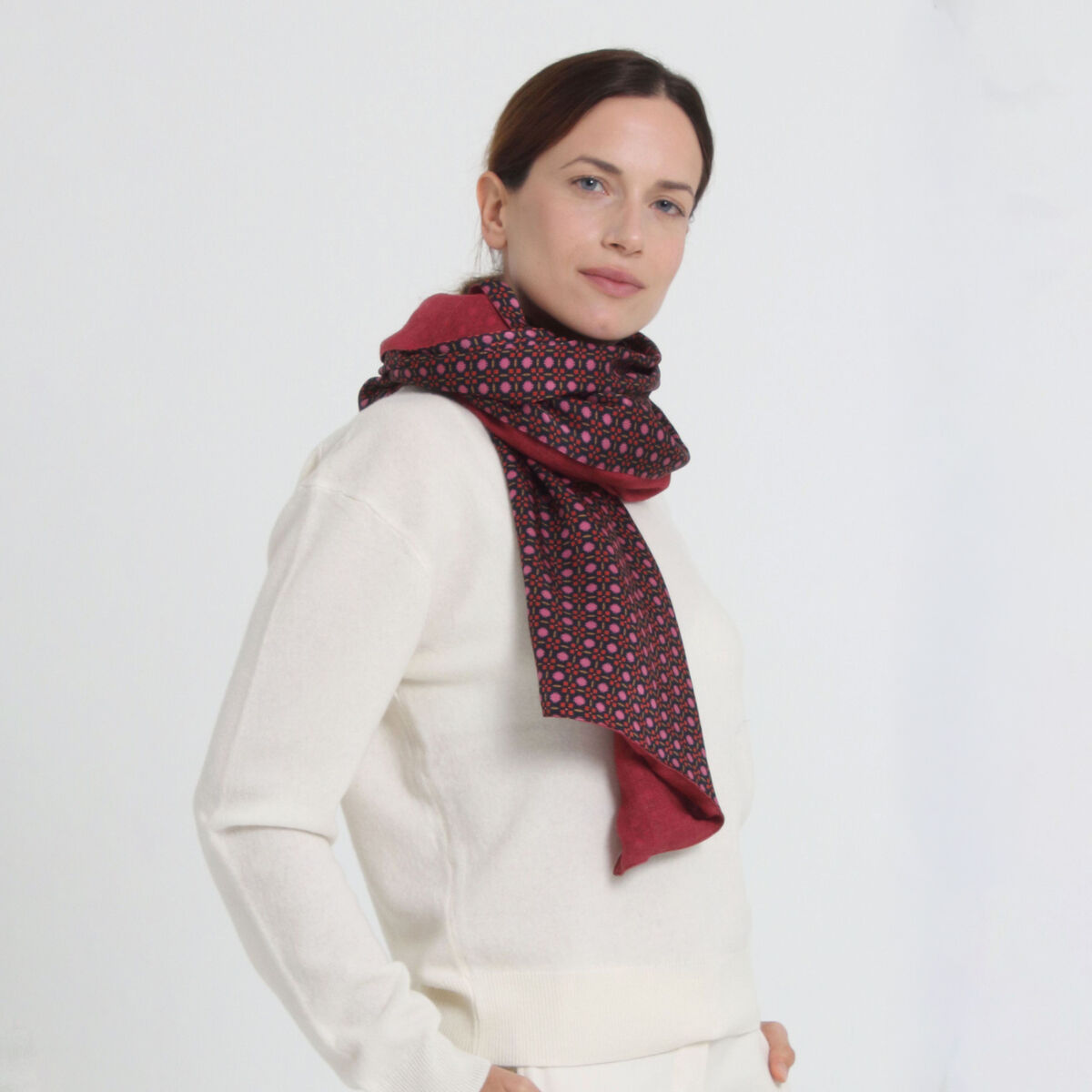 Frau mit hellem Pullover trägt den Wolle-Seidenschal »Liv« in Pink von Shalls Barcelona. Der Schal zeigt ein florales Muster in Rot, Pink und Dunkelblau auf dunklem Grund, ist locker um den Hals gelegt und hebt sich elegant vom weißen Hintergrund ab.