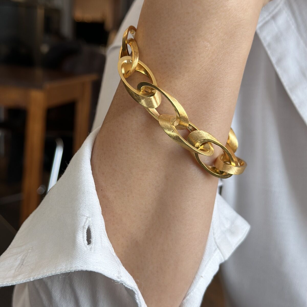 Ein elegantes Armband aus Silber, das feingoldplattiert ist, getragen von einer Person in einem weißen Hemd. Das Armband hat ein Kettendesign mit goldener Farbe.