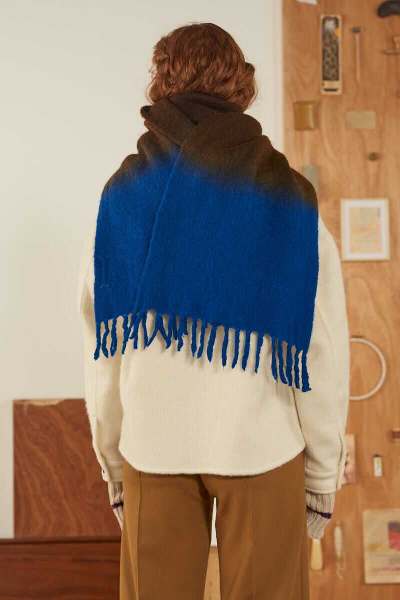 Rückansicht einer Person in einem beigen Pullover, die einen Schal „No.698“ trägt. Der Schal hat einen Farbverlauf von tiefem Blau zu Braun und ist mit Fransen versehen.