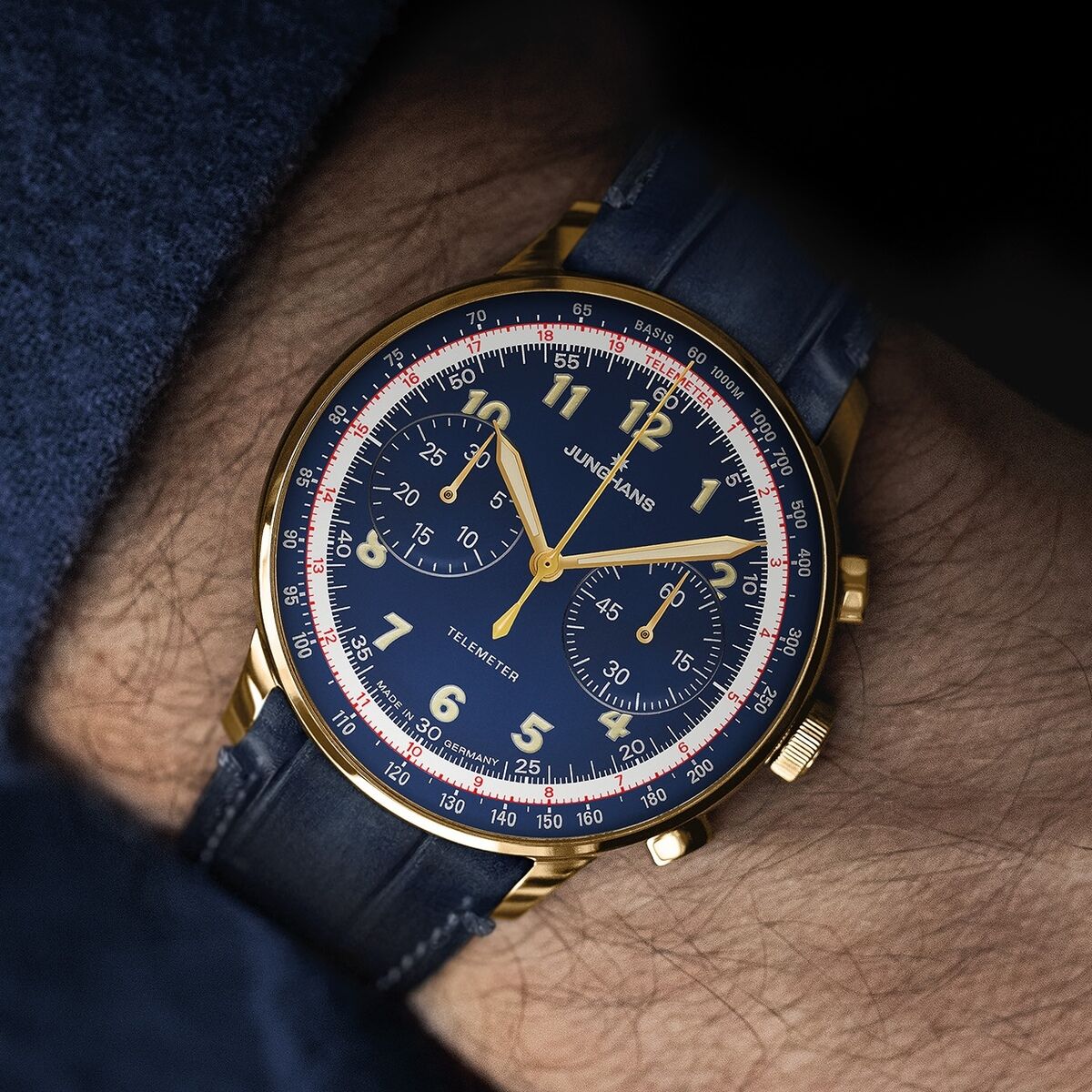 Nahaufnahme einer hochwertigen Junghans ZEIT-Sonderedition »Telemeter« Armbanduhr am Handgelenk. Die Uhr hat ein mitternachtsblaues Zifferblatt, goldfarbene Zeiger und Ziffern, ein blaues Lederarmband und eine rote Telemeterskala. Hochwertige Verarbeitung im sportlich-eleganten Look.
