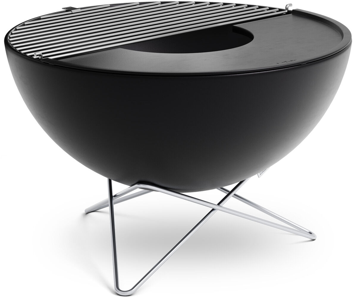 Ein stilvoller Grillrost aus Edelstahl, montiert auf einer schwarzen, halbkugelförmigen Basis mit stabilen Metallbeinen, die den Grill anheben. Dieser tragbare 'BOWL Grillrost' eignet sich perfekt für Outdoor-Events.