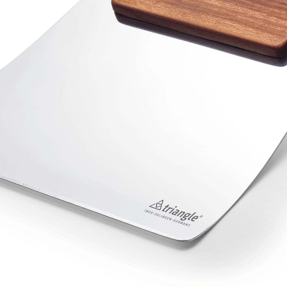Eine Gemüseschaufel der Marke triangle liegt auf einer hellen Arbeitsfläche. Die Schaufel hat eine silberne, flache Edelstahlklinge und einen schwarzen, ergonomischen Kunststoffgriff. Das Produkt wirkt stabil, glänzt leicht und ist modern designt.