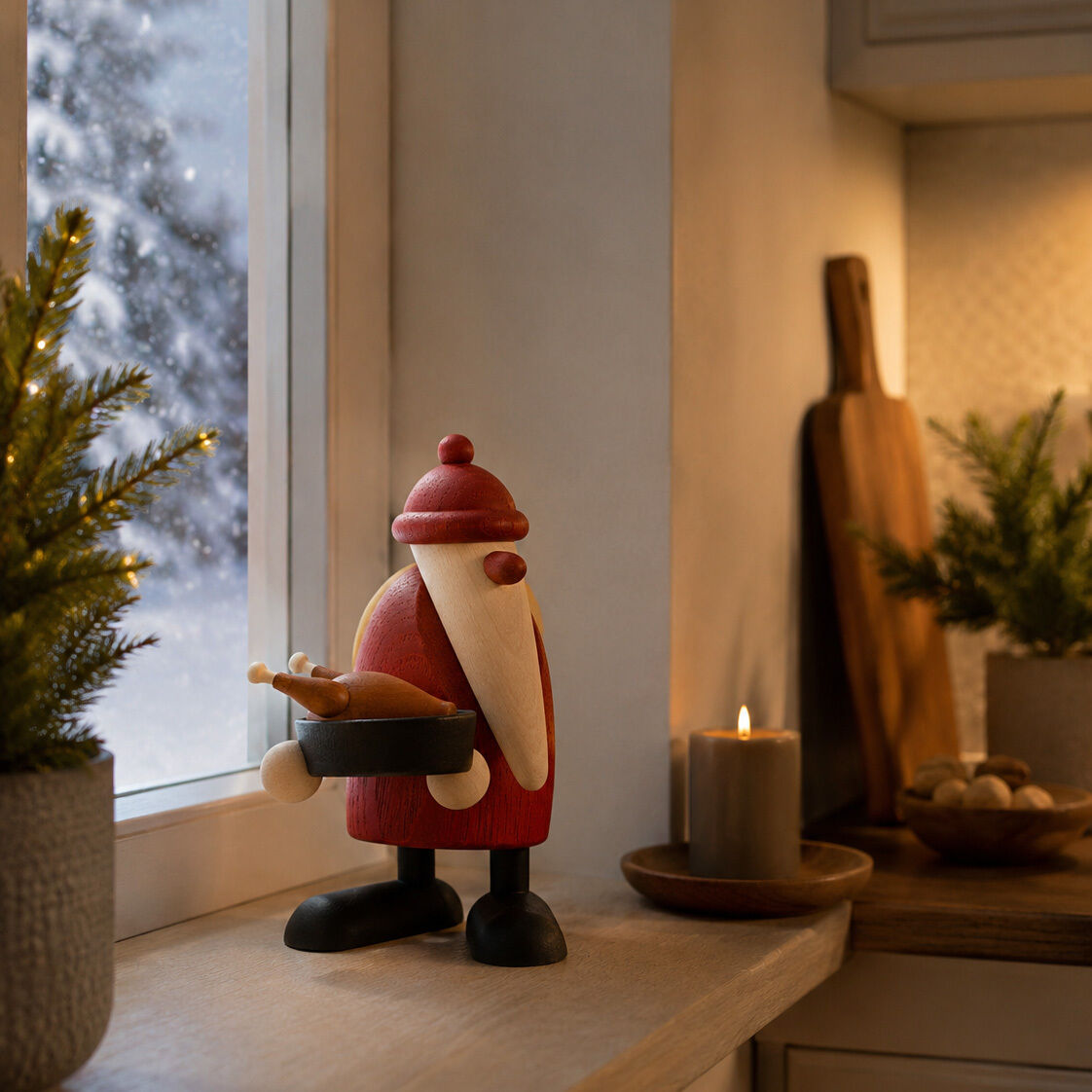Handgefertigte Holzfigur „Weihnachtsmann mit Gänsebraten“ von Björn Köhler auf einem Fensterbrett in einer festlich eingerichteten, gemütlichen Küche. Der Weihnachtsmann trägt rote Kleidung, hält eine Pfanne mit gebratener Gans und steht zwischen Tannenzweigen und Kerze.