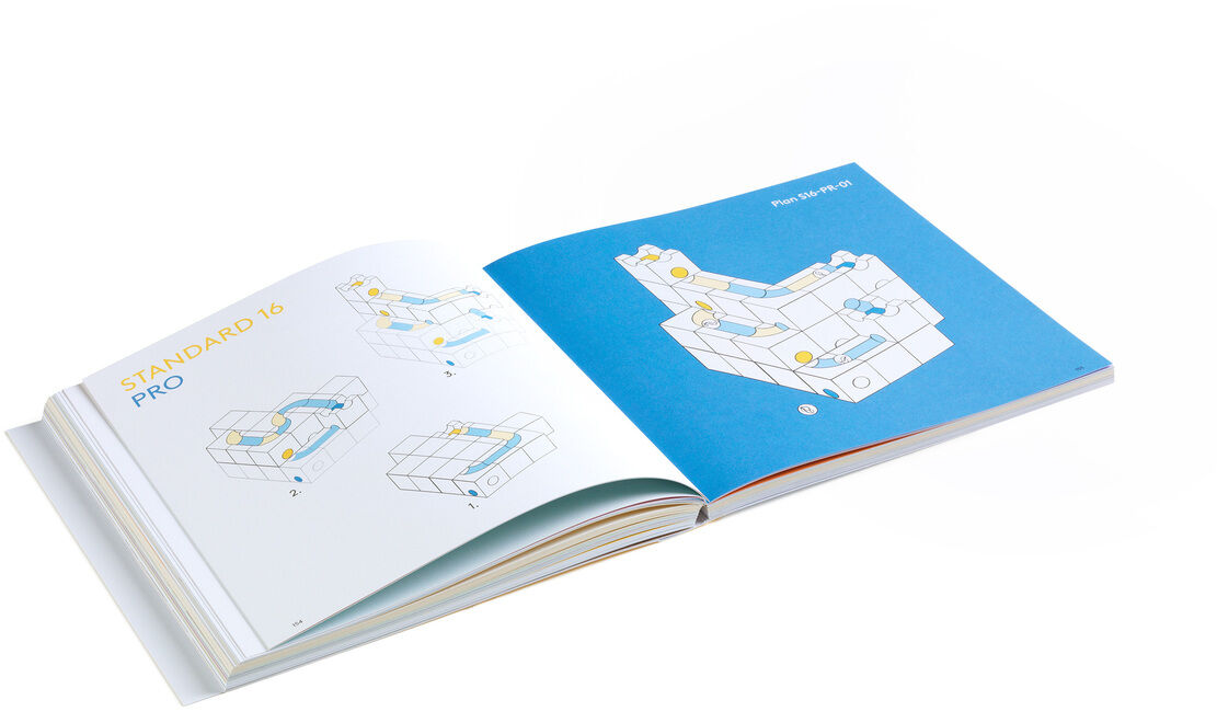 Ein aufgeschlagenes Buch zur Kugelbahn mit dem Titel »CUBORO - DAS BUCH«. Das Buch enthält farbige Illustrationen und Baupläne zum Erstellen von Kugelbahnen mit CUBORO-Bausteinen.