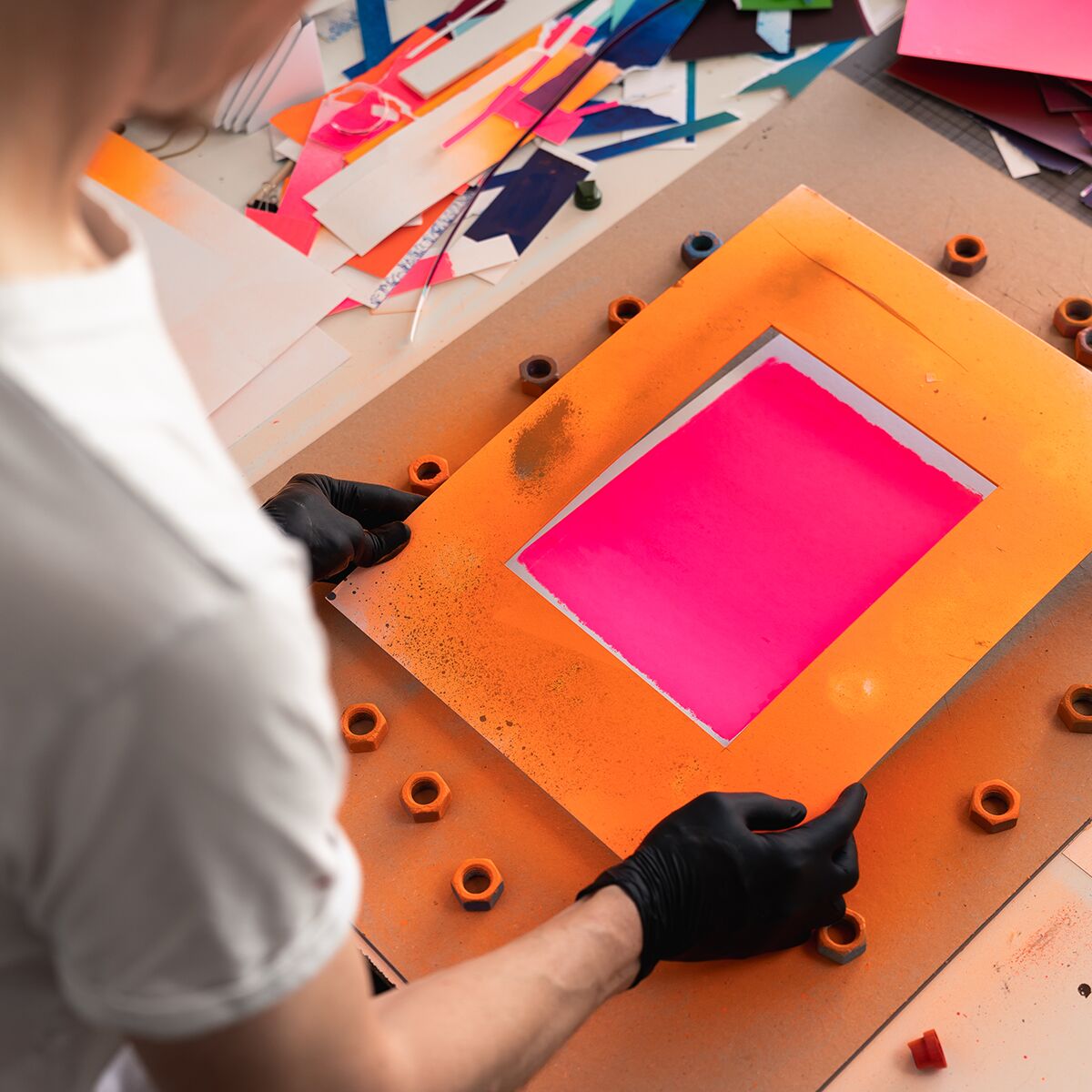 Ein kreatives Kunstwerk der ZEIT-Sonderedition Imagine ist zu sehen. Das Bild zeigt ein Originalwerk in kräftigen Pink- und Orangetönen auf einem Tisch, umgeben von Bastelmaterialien und Papierzuschnitten. Eine Person arbeitet gerade an dem Kunstobjekt. Die Szene vermittelt eine moderne, künstlerische Atmosphäre und betont handgemachte, dekorative Elemente.