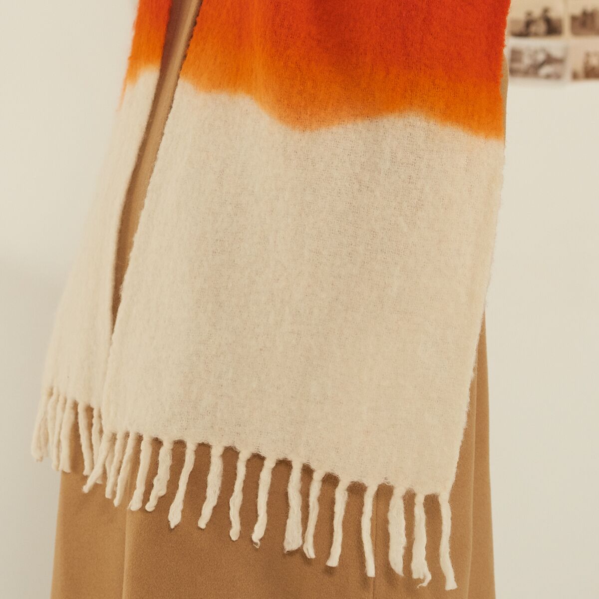 Detailaufnahme eines eleganten Schals »No. 698« von MOISMONT aus hochwertiger Schurwolle und Nylon. Der Schal zeigt intensive Farbübergänge von leuchtend orange-rot zu cremefarben und besitzt ungeordnete, feine Fransen an der Kante. Hintergrund neutral, Fokus auf Textur und Farben.