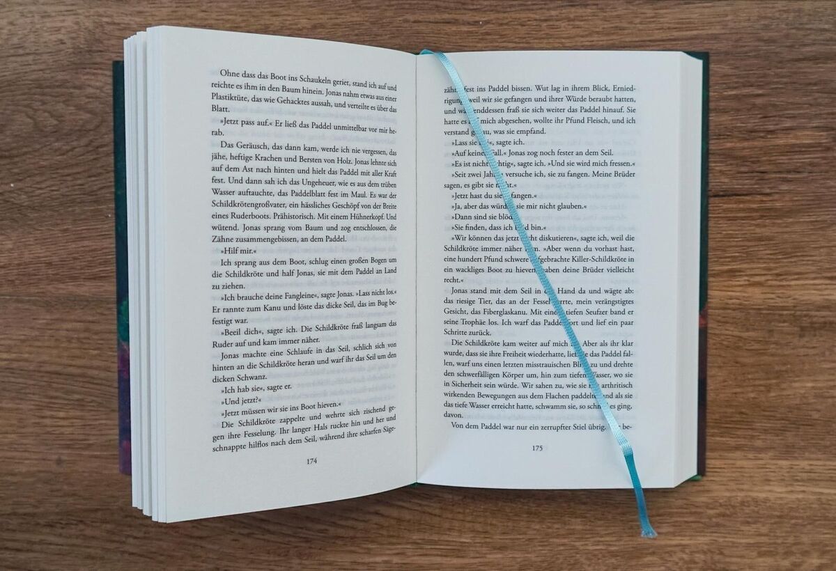 Ein aufgeschlagenes Buch namens 'Cowley Heller, Miranda: Der Papierpalast' liegt auf einem Holztisch. Ein hellblaues Lesezeichen hängt aus den Seiten.